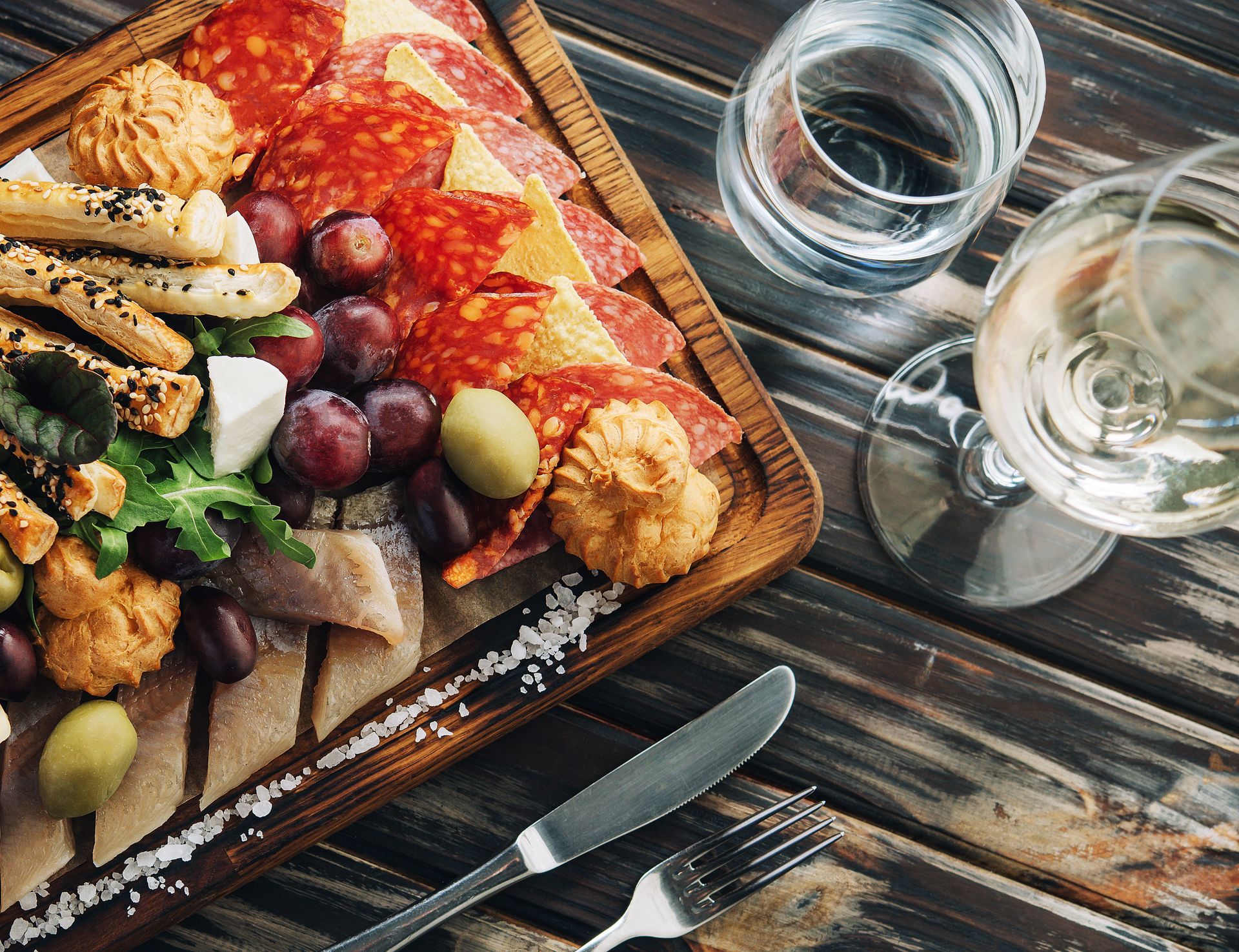 Charcuterie board with meats, cheeses, grapes, and crackers, next to wine and water glasses.