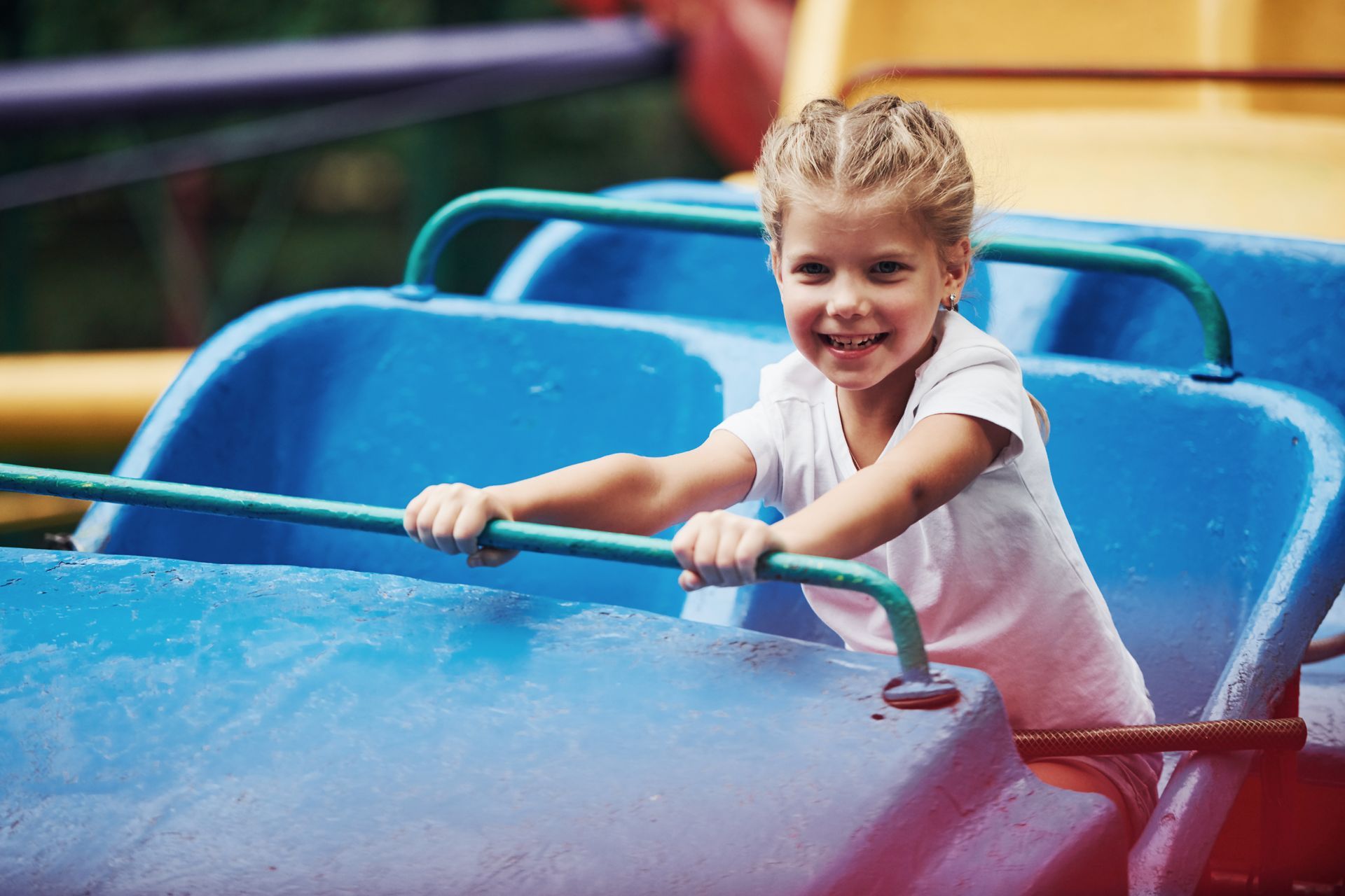 Smiling child on a blue amusement park ride, holding onto a bar.