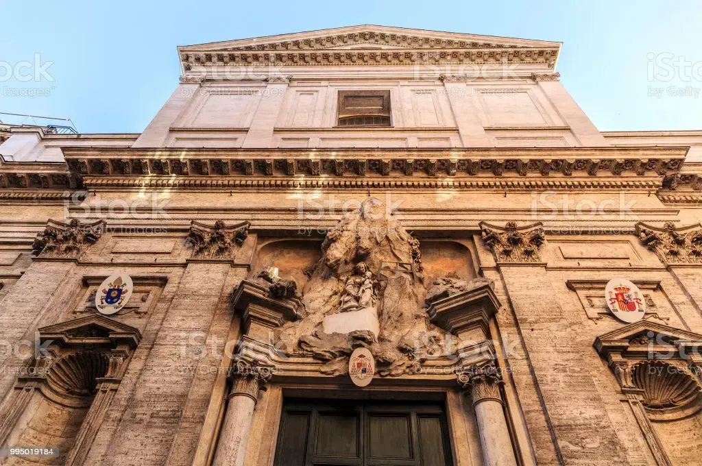 Low-angle view of a beige stone church facade with ornate carvings, columns, and a doorway.
