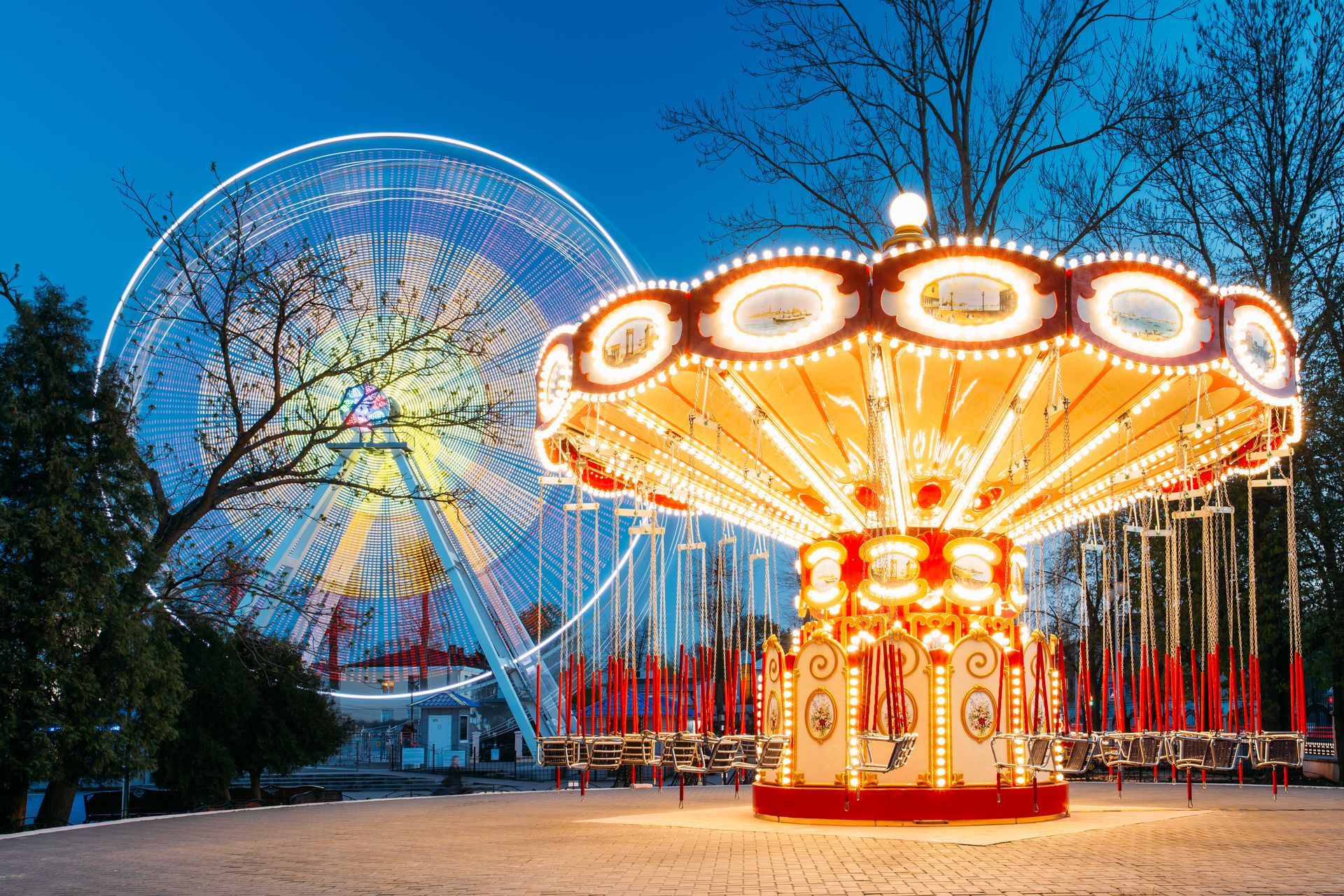 Ferris wheel and carousel at an amusement park lit up at night, against a dark blue sky.