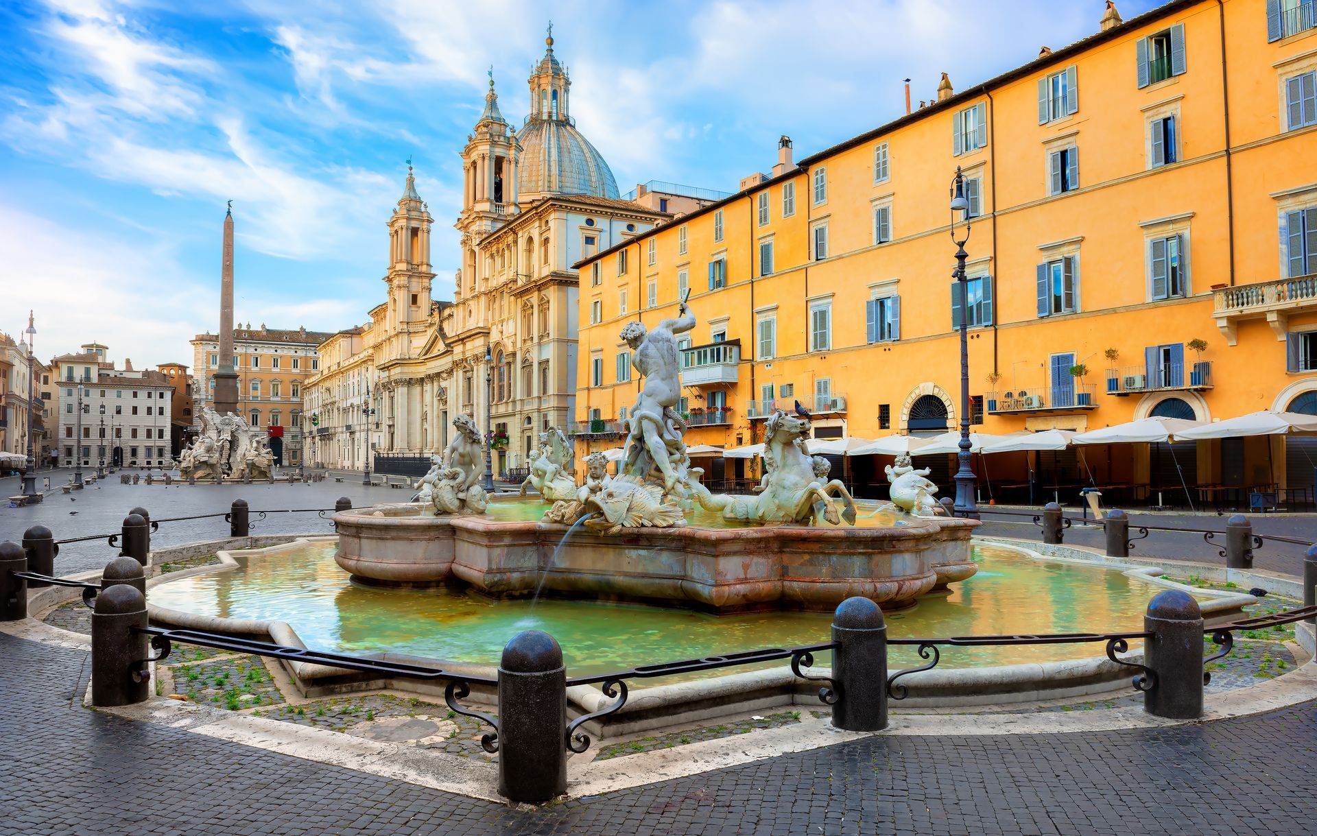 Piazza Navona in Rome with the Fountain of Four Rivers in foreground. Buildings and an obelisk in the background.