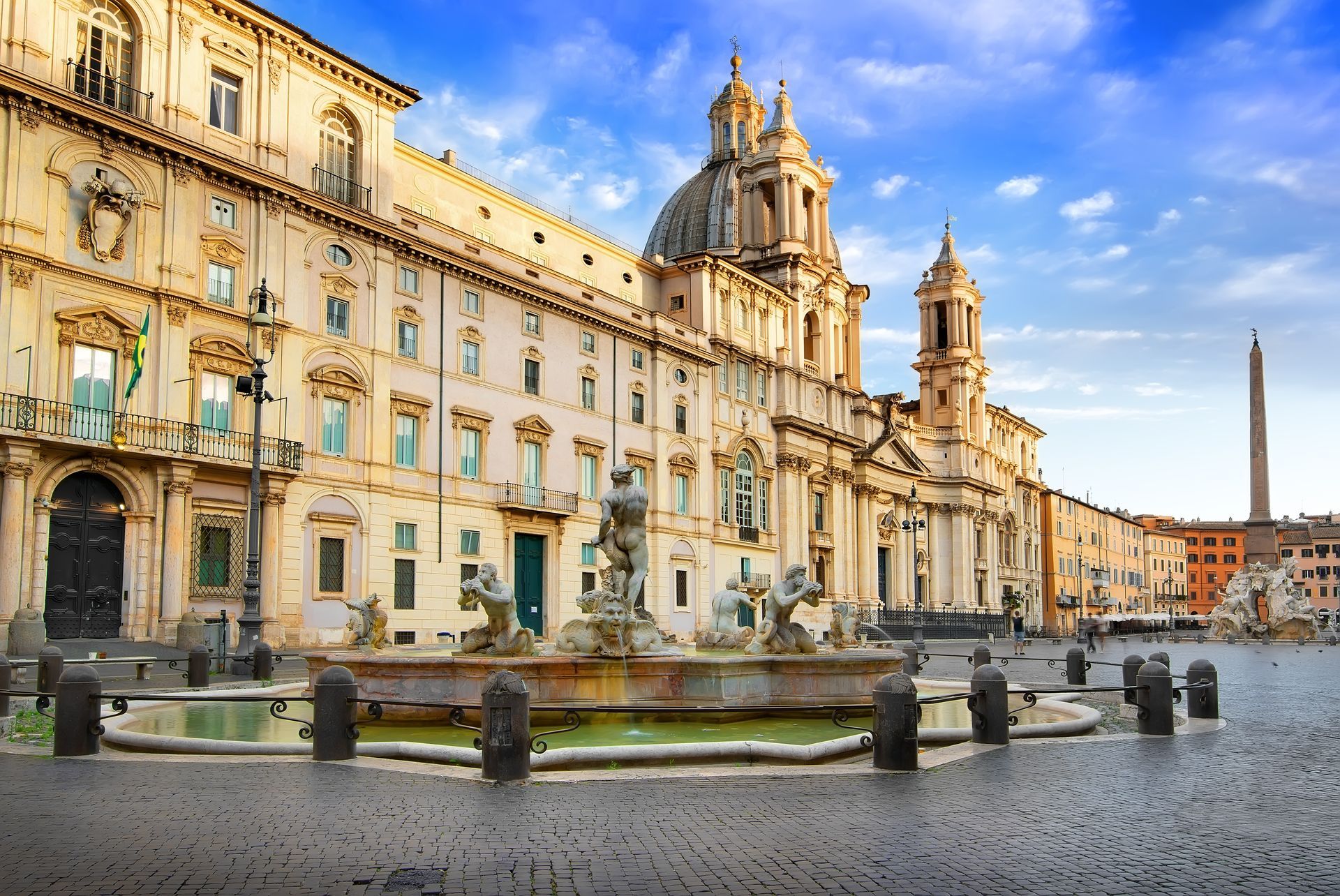 Piazza Navona, Rome: ornate fountain in cobblestone square, buildings, obelisk, blue sky.