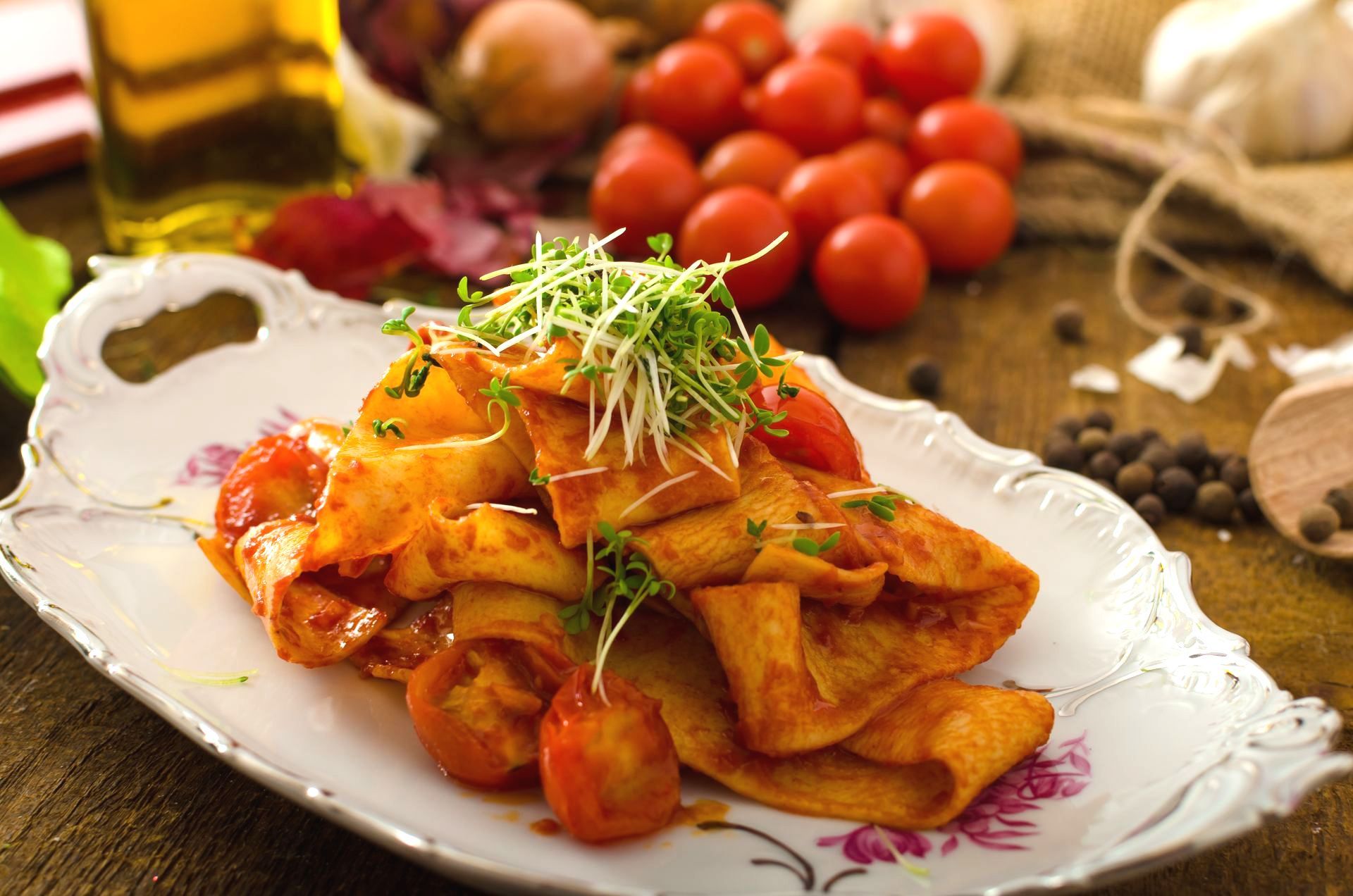 Pasta dish with tomato sauce, cherry tomatoes, and sprouts on a decorative plate.