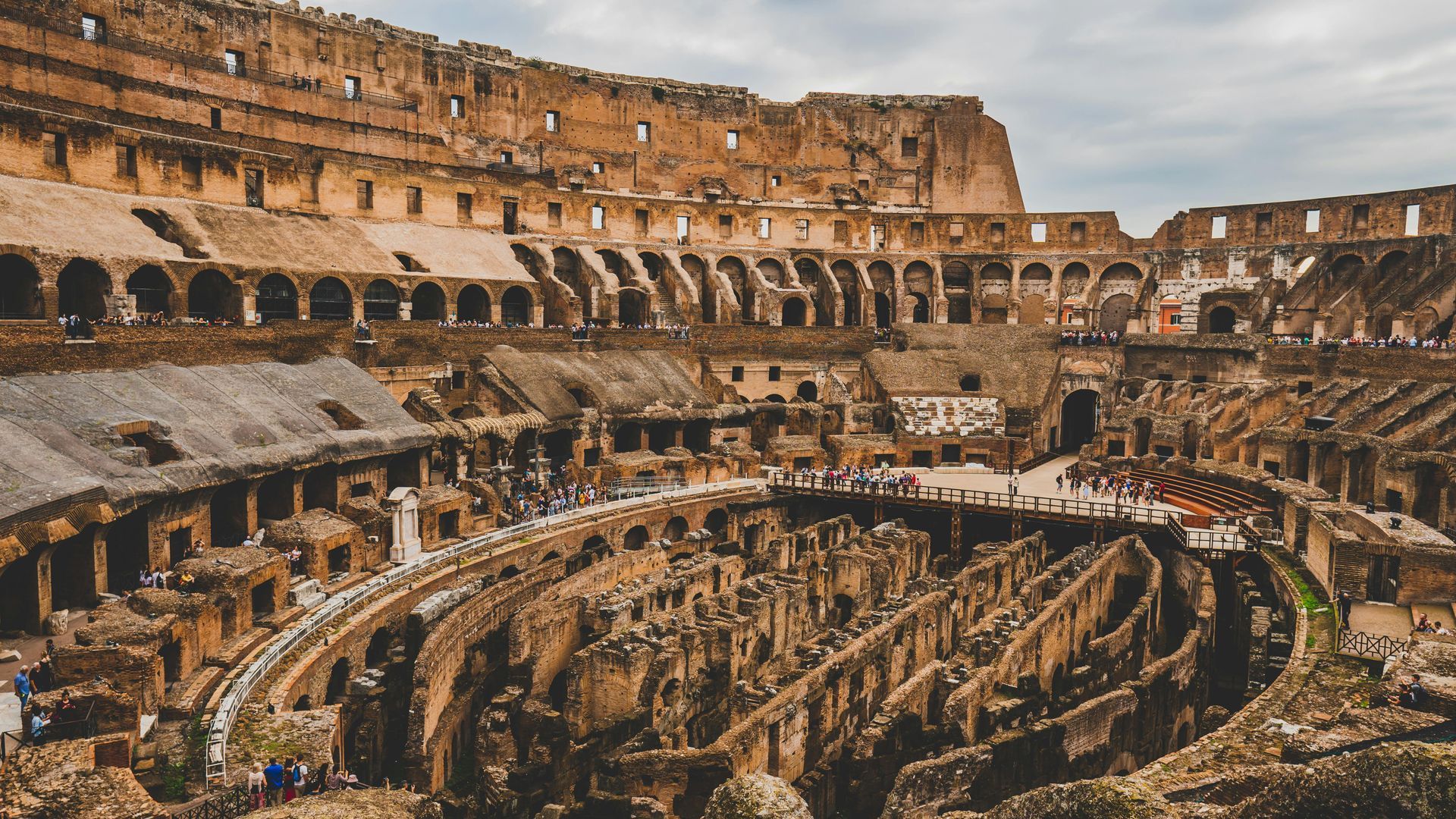 Inside view of the Colosseum in Rome, Italy, with arches, ruins, and people touring.