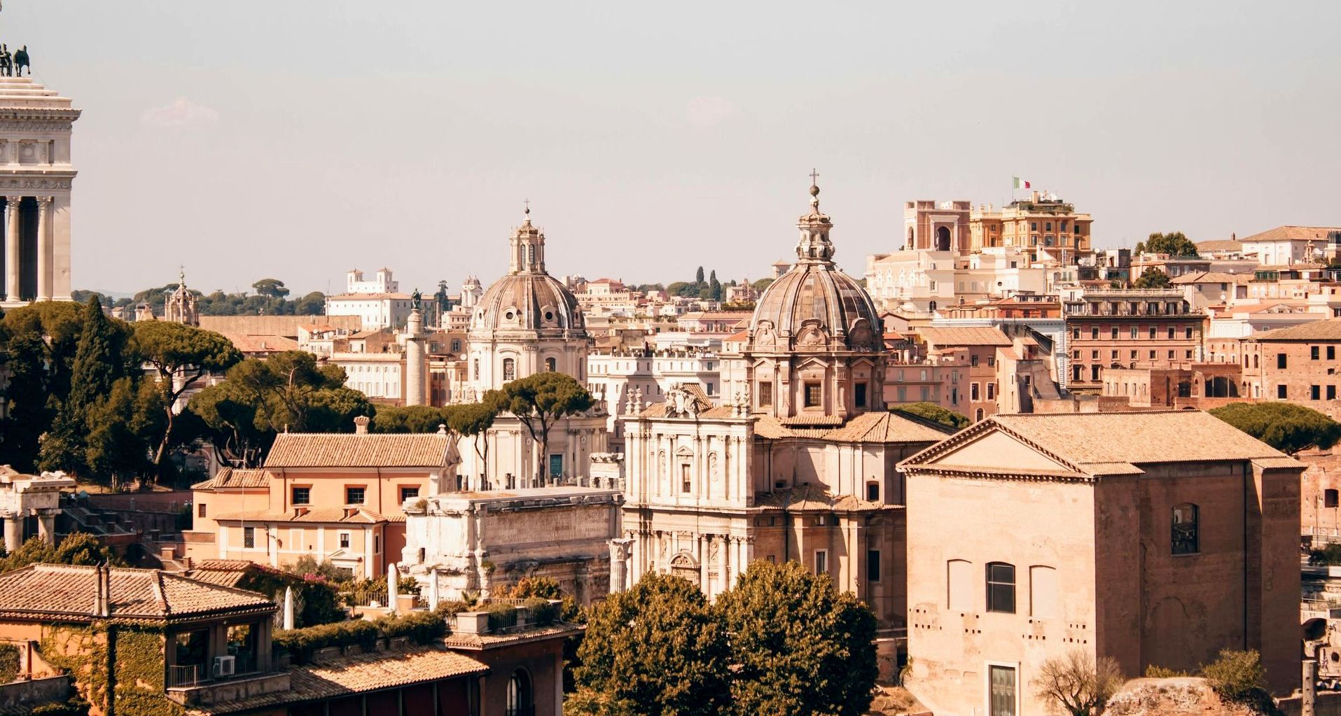 Cityscape of Rome, Italy, with historic buildings, domes, and warm sunlight.