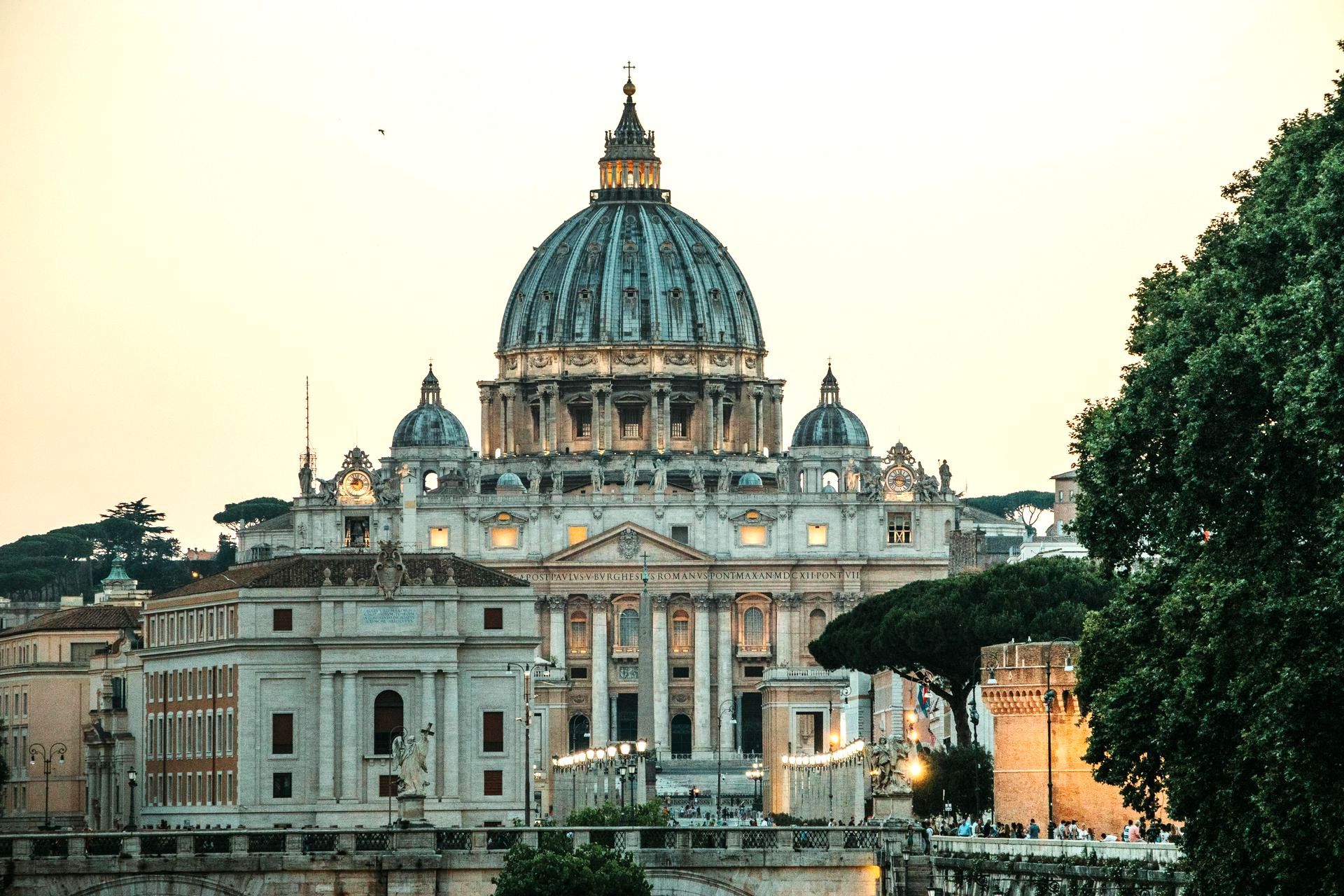 St. Peter's Basilica, Rome, with its iconic dome, lit against an evening sky.