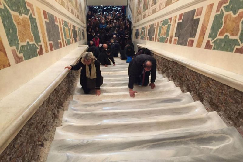 People crawling up marble stairs; others watch from above.