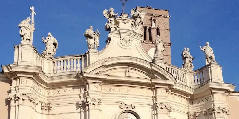 Baroque church facade with statues and a tall bell tower against a blue sky.