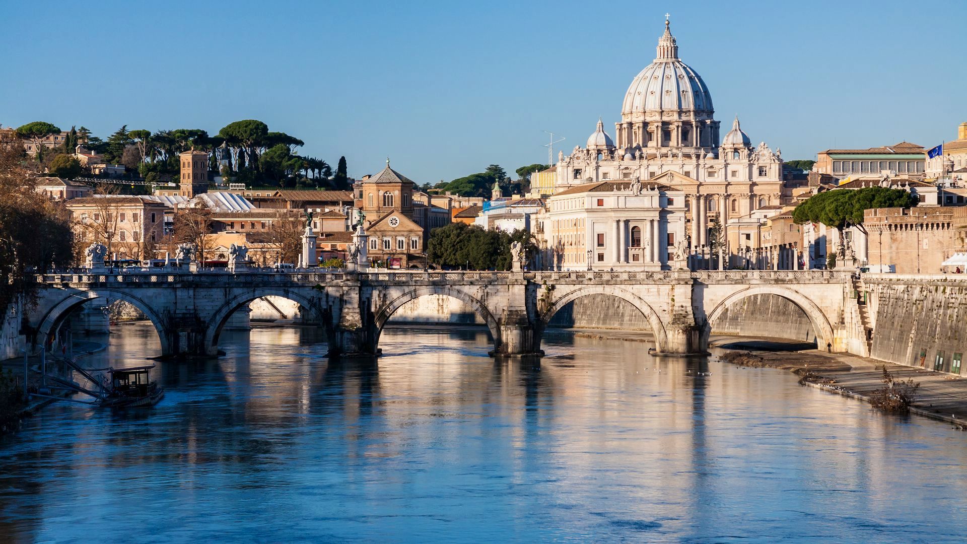 St. Peter's Basilica overlooking the Tiber River in Rome, Italy, with bridges and buildings.