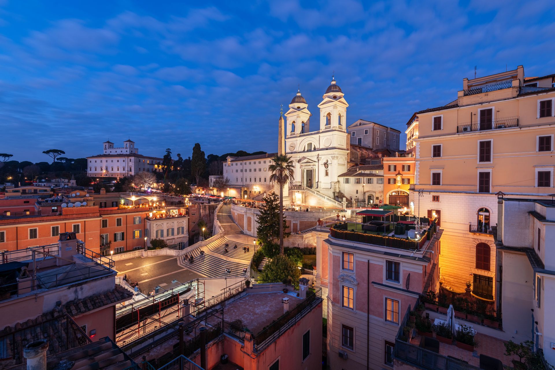 Spanish Steps and fountain in Rome at dusk. Buildings frame the stairs leading to a church.