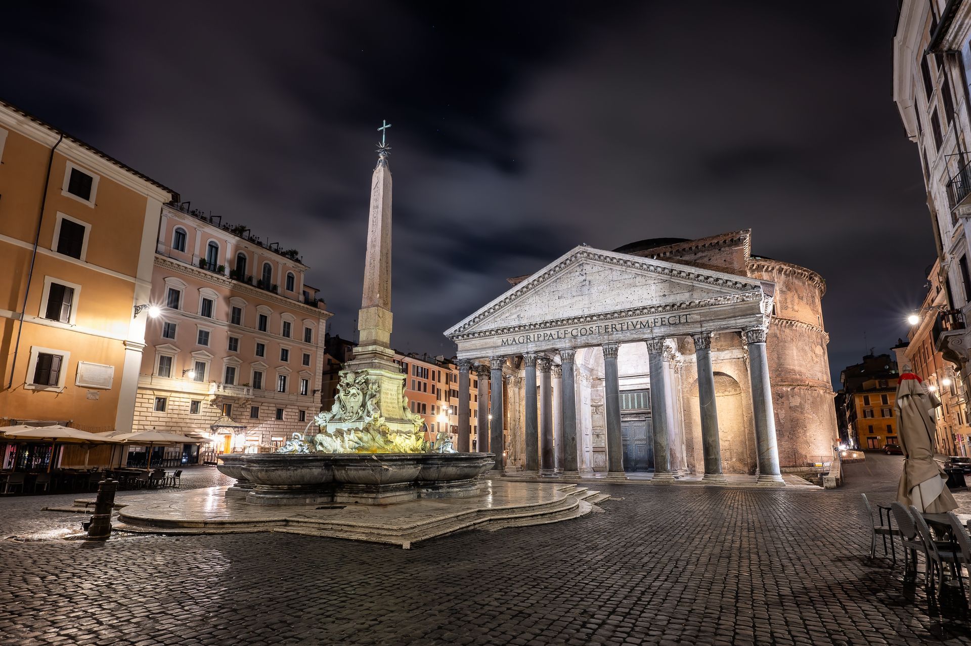 Pantheon at night, Rome, illuminated facade and fountain with obelisk, cobblestone plaza, buildings in background.