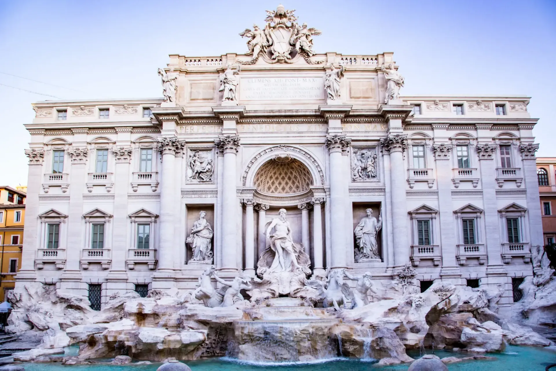 Trevi Fountain in Rome: Baroque architecture with sculptures, water flowing into a turquoise pool, under a clear sky.