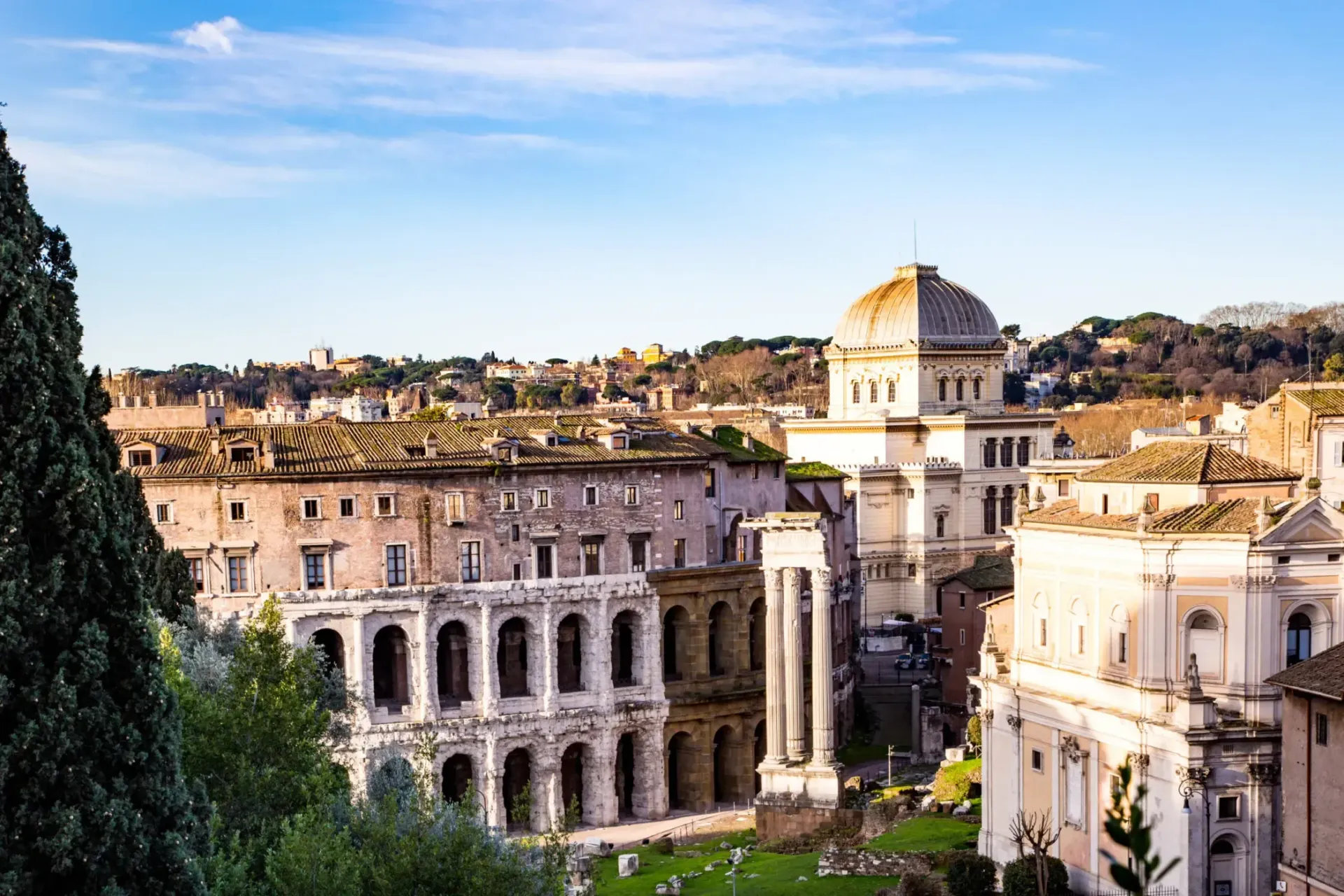 Ruins and buildings in Rome with a prominent domed structure under a blue sky.