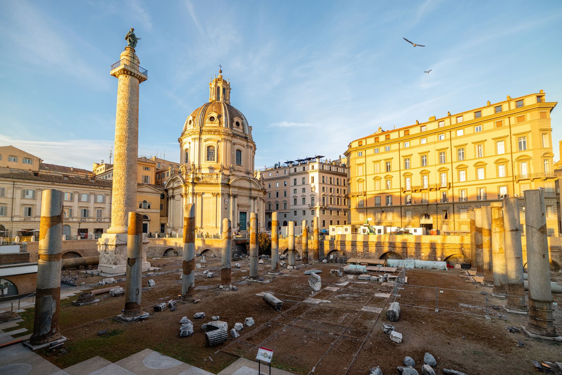 Ancient Roman ruins in Rome, Italy, with a towering column and church under a blue sky.