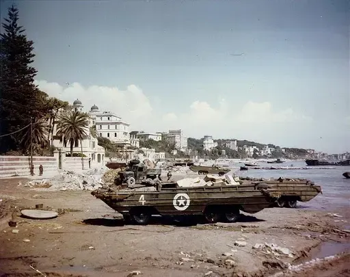 Amphibious vehicle on a beach, buildings in the background. Bright sky, sunny day.