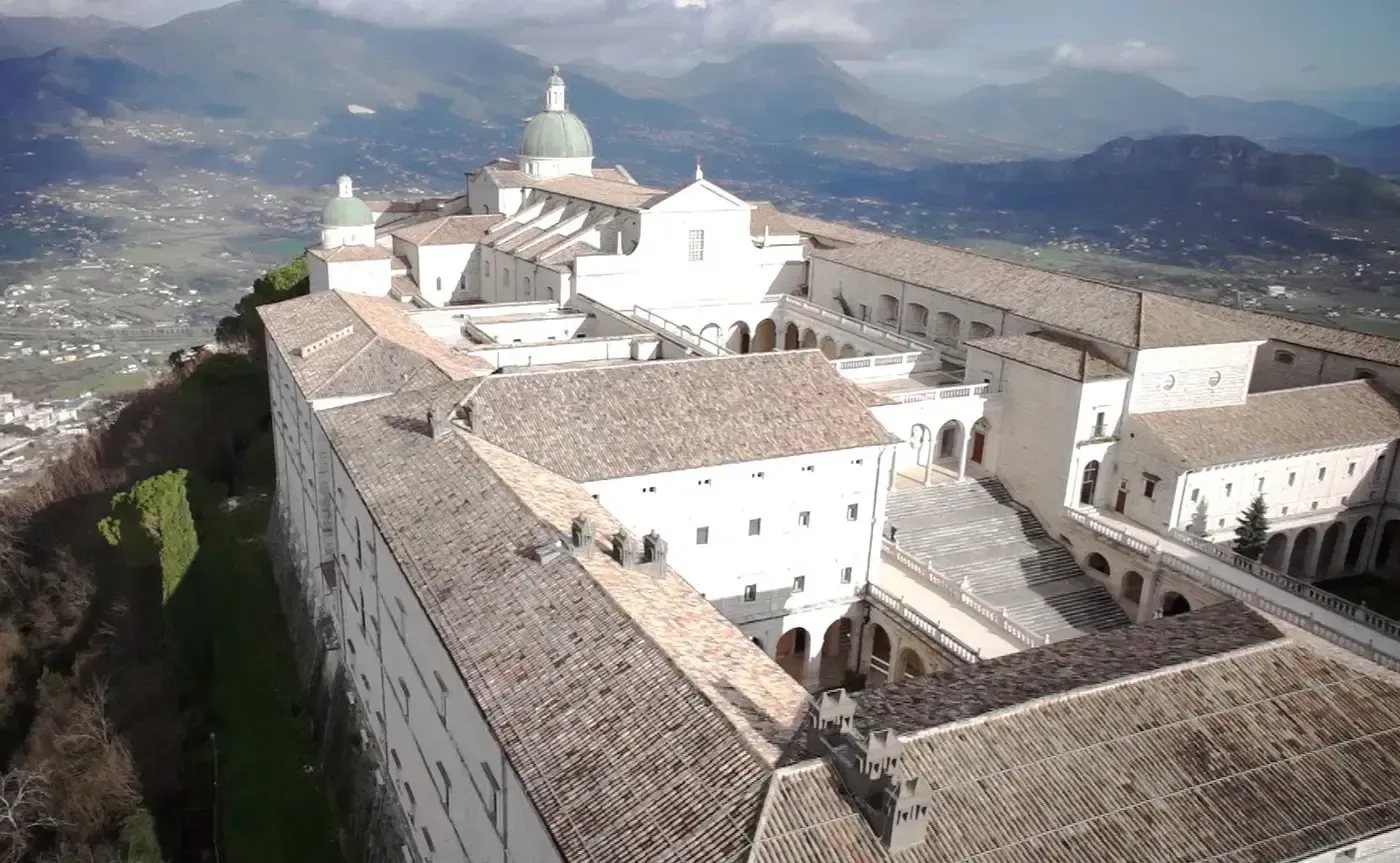 Large white monastery complex on a hilltop, with surrounding mountains in the background.