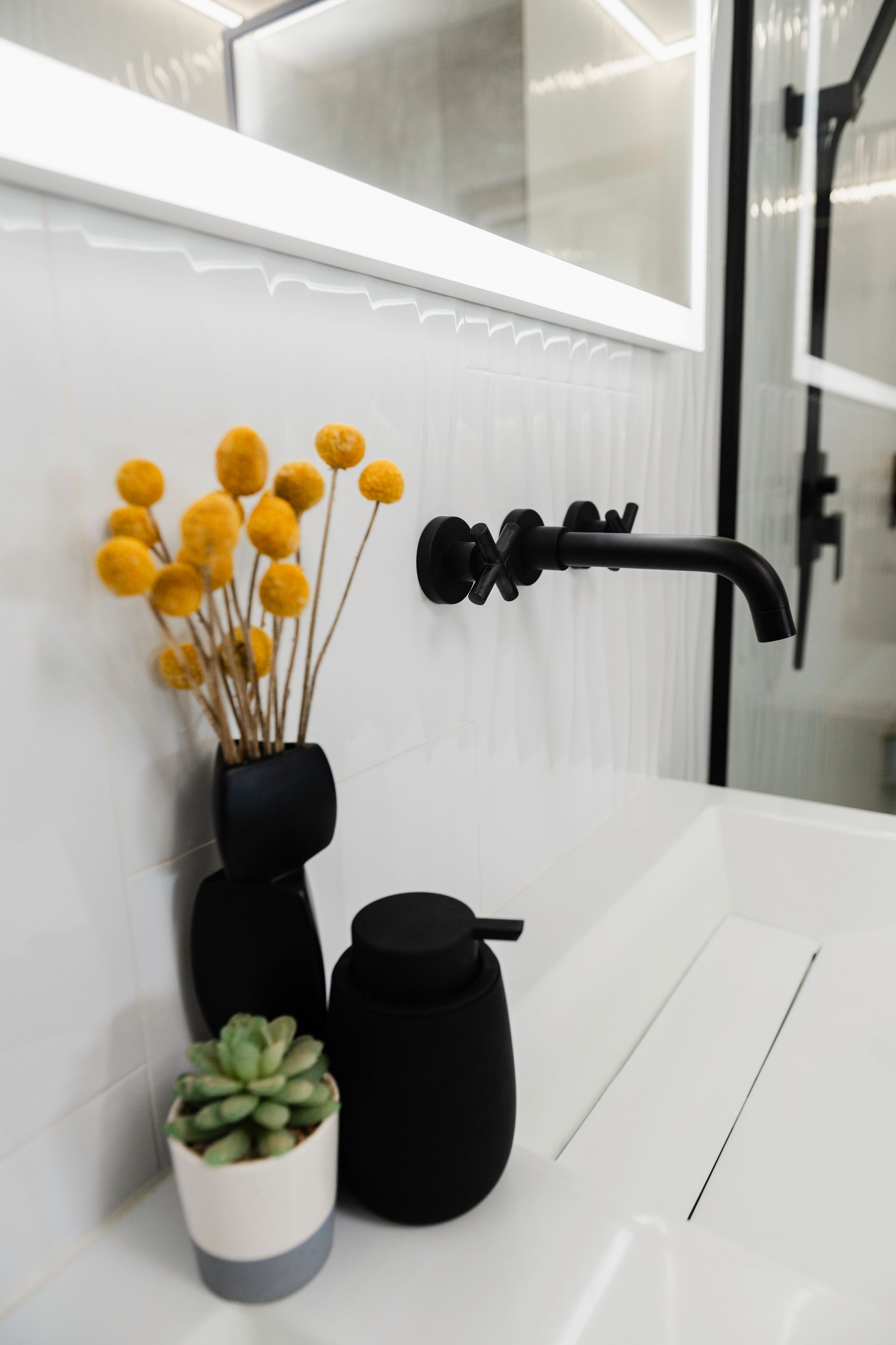 A bathroom sink with a vase of yellow flowers and a black soap dispenser.