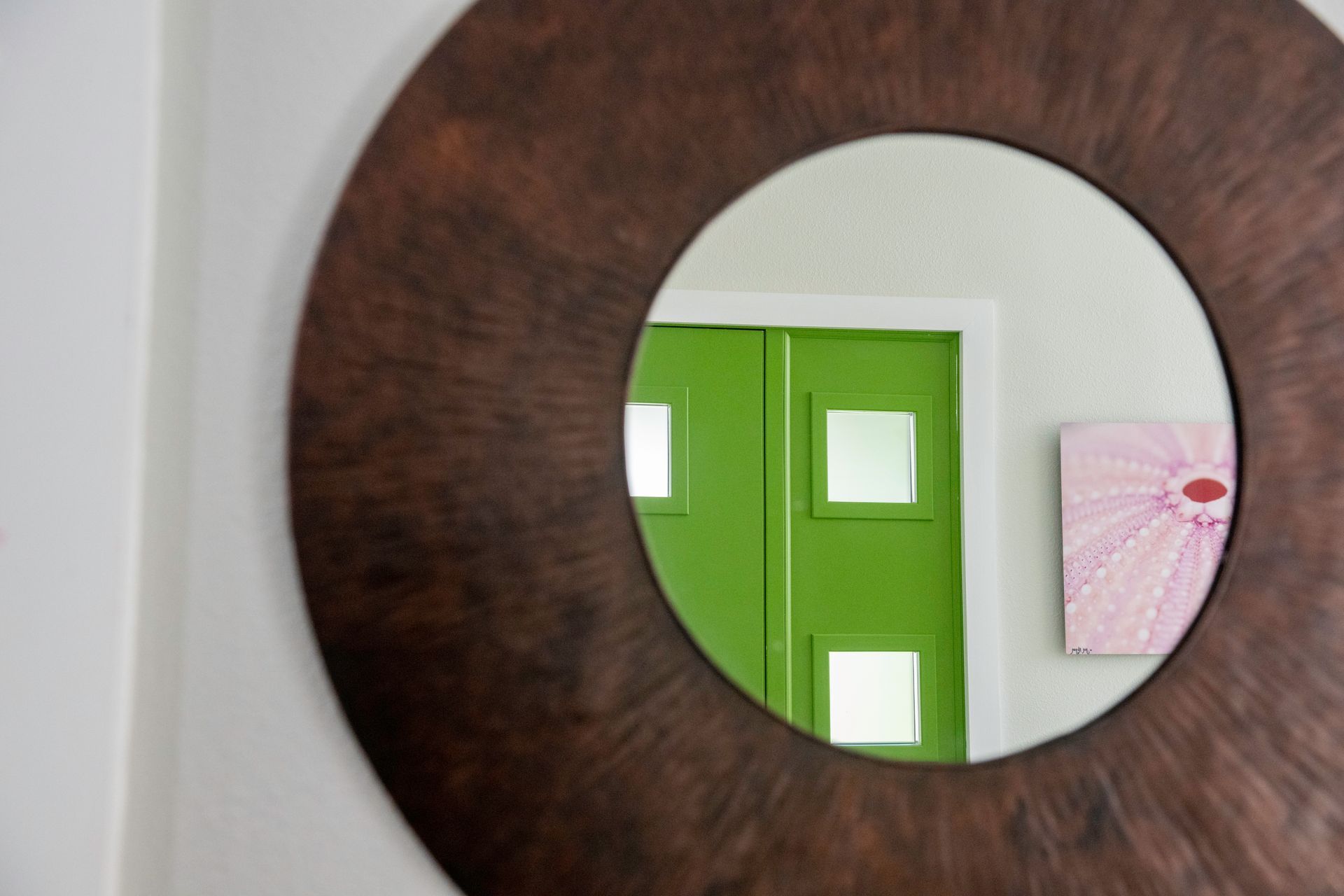 A round mirror with a brown frame is hanging on a wall.