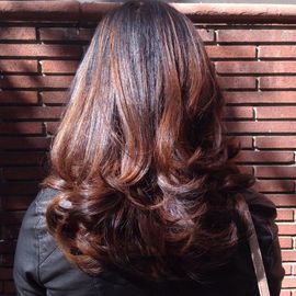 A woman with long brown hair is standing in front of a brick wall