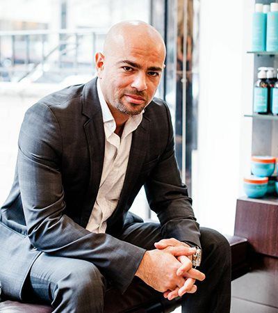 A man in a suit is sitting on a bench with his hands folded