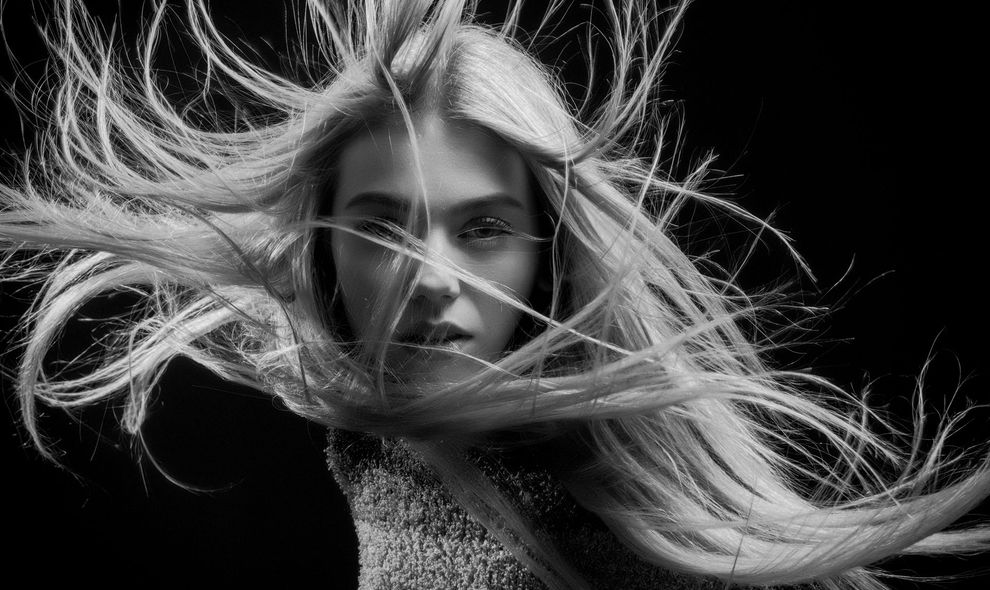 A black and white photo of a woman with long blonde hair blowing in the wind.