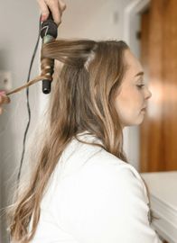 A woman is getting her hair curled with a curling iron.