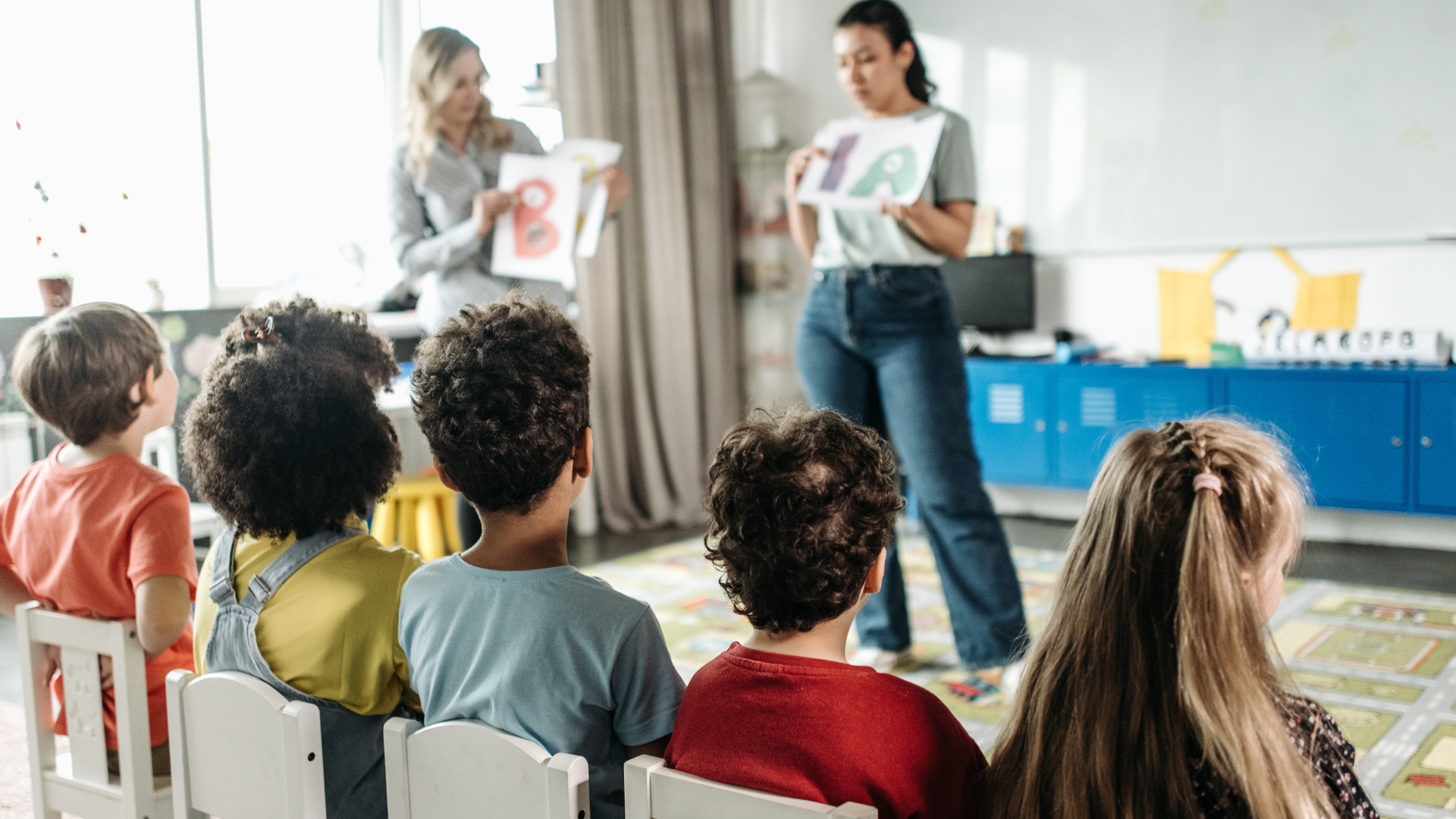 A group of children are sitting in a classroom listening to a teacher.