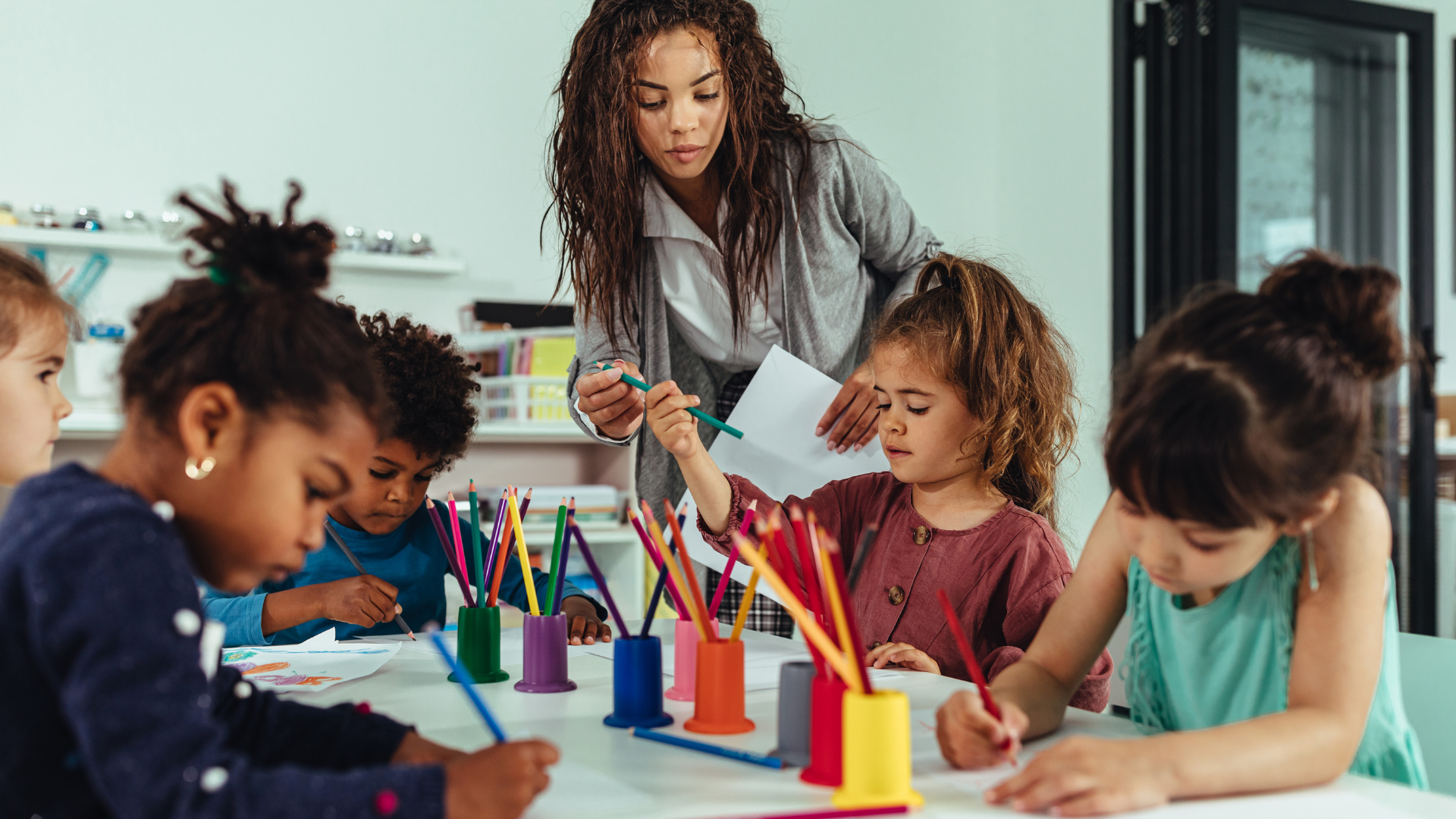 A group of children are sitting at a table with their teacher.