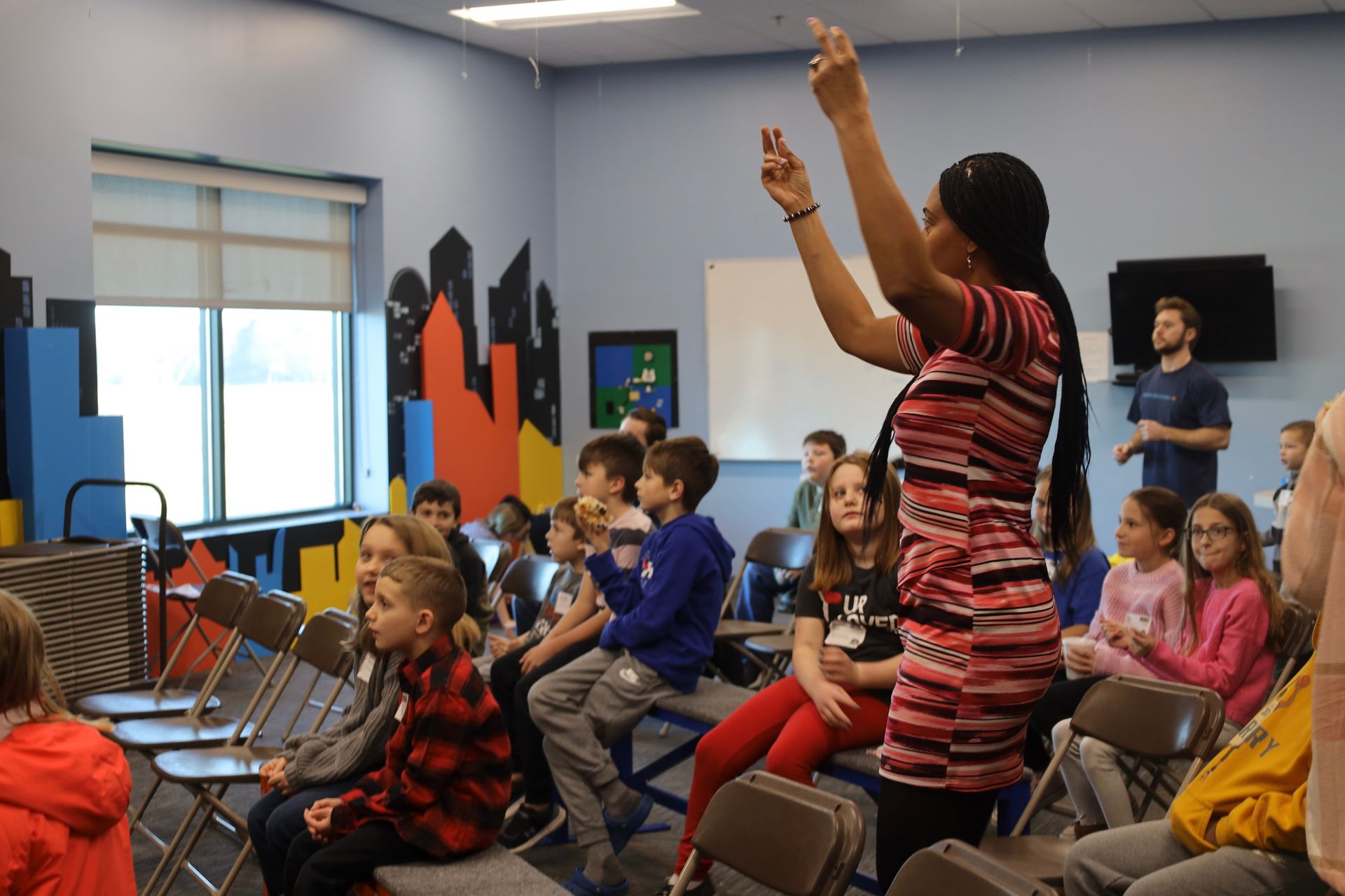 a woman is talking to a group of children sitting in chairs .