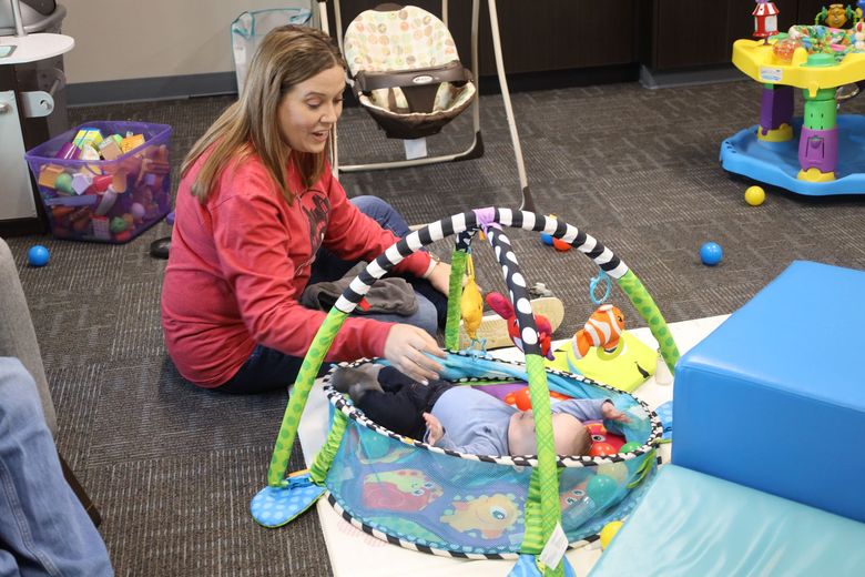 a woman is sitting on the floor playing with a baby in a play mat .