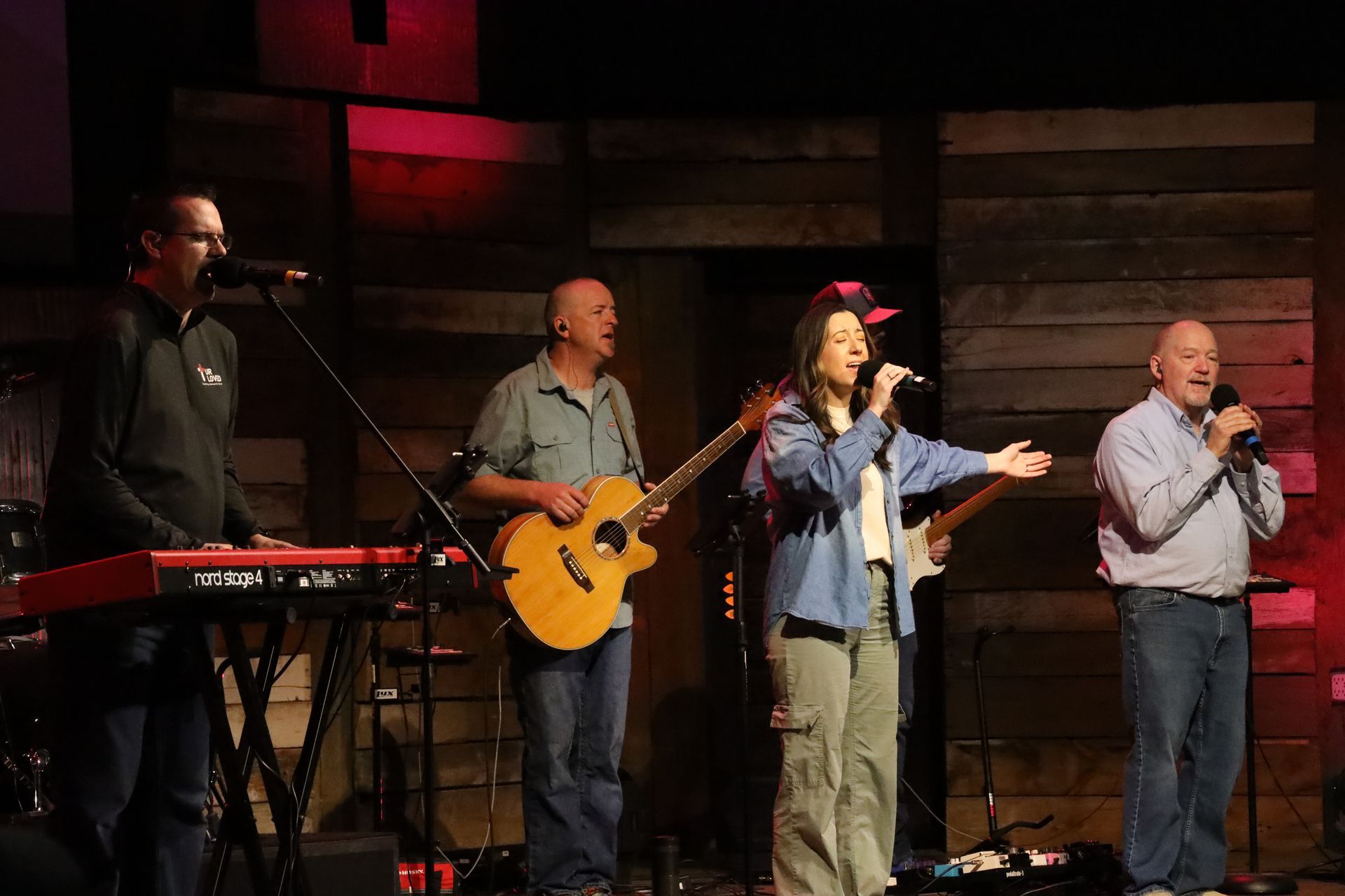 a group of people are standing on a stage singing into microphones .