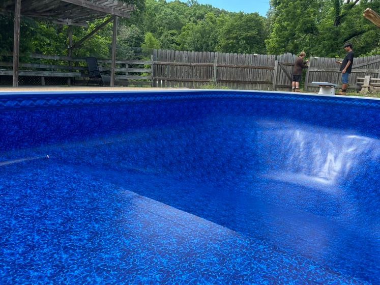 A man is standing next to a blue swimming pool.