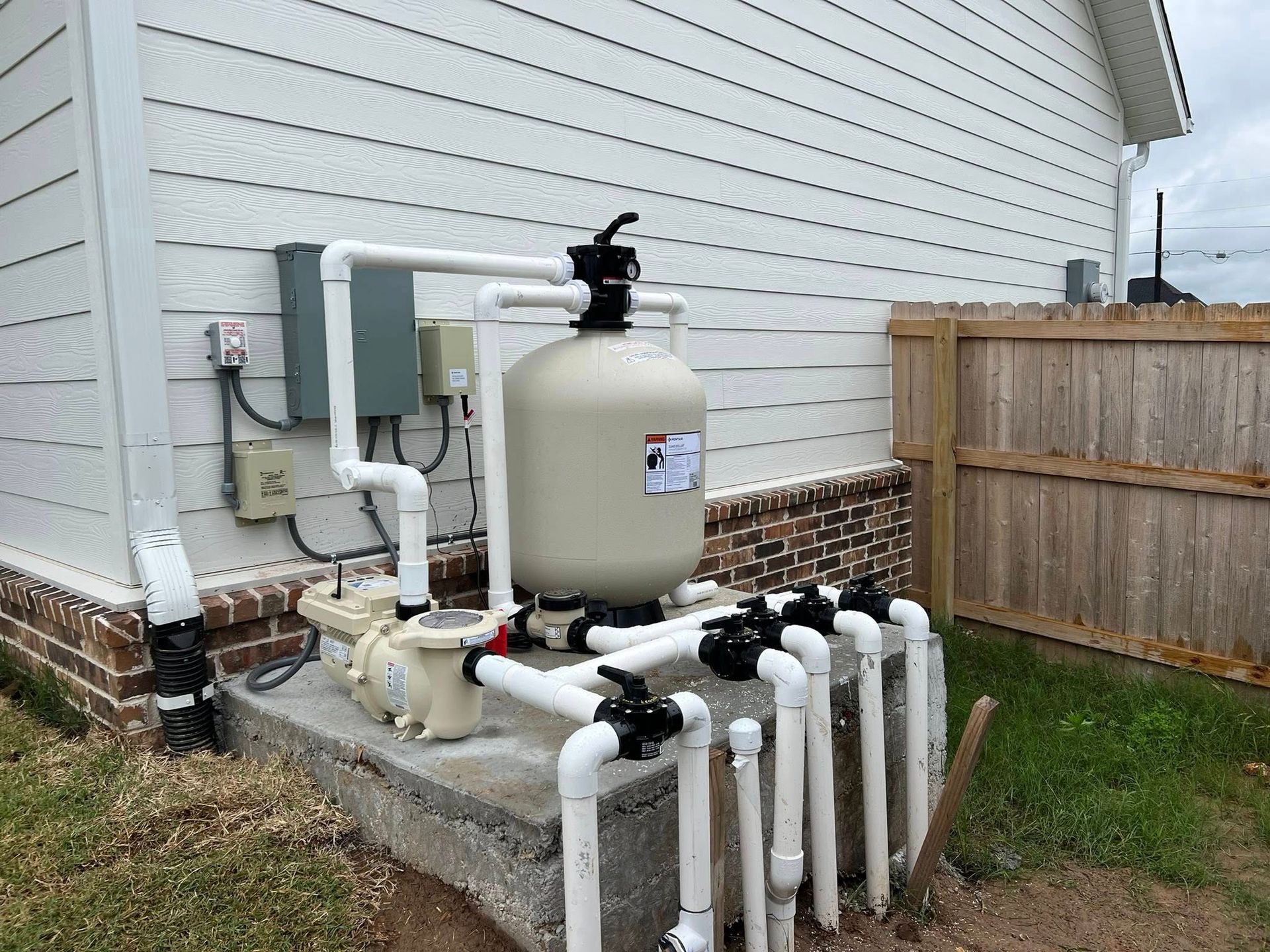 A pool filter is sitting on the side of a house next to a fence.