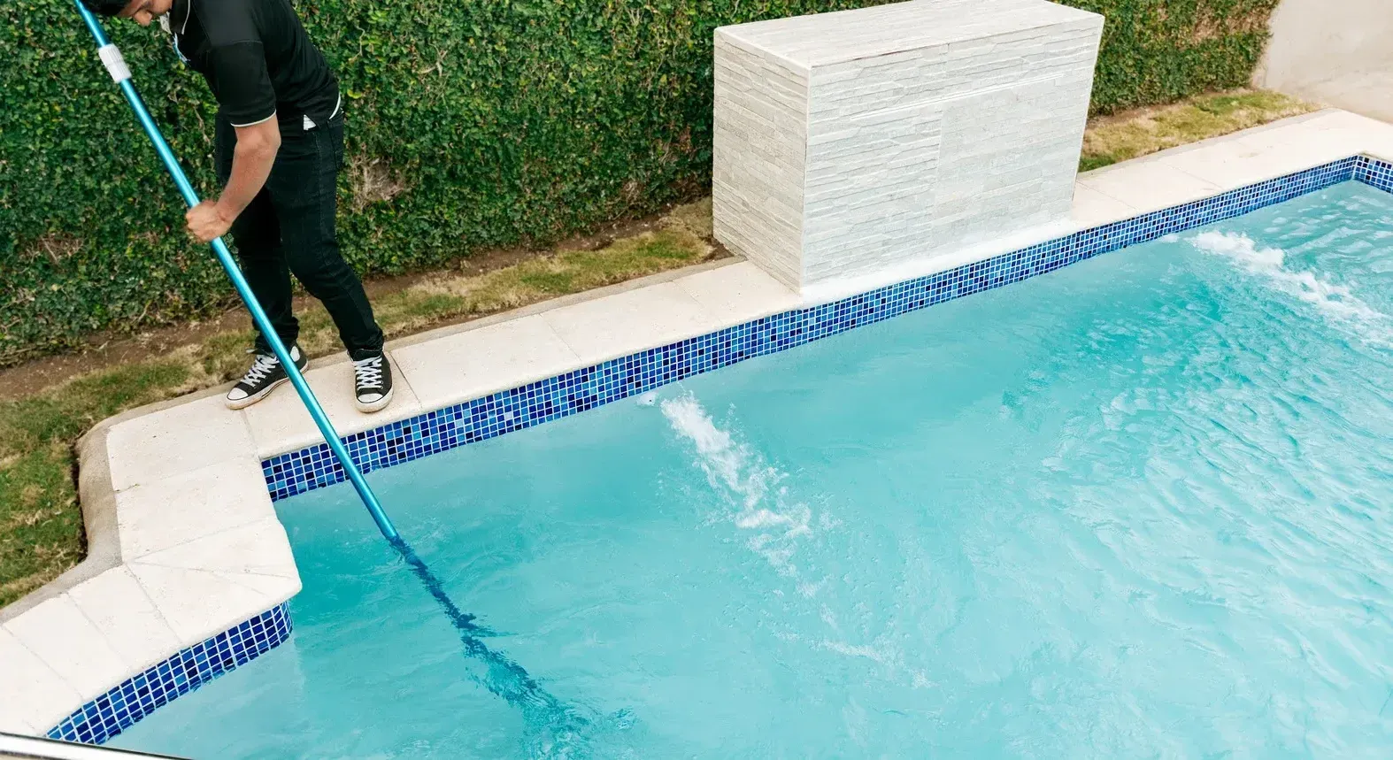 A man is cleaning a swimming pool with a broom.