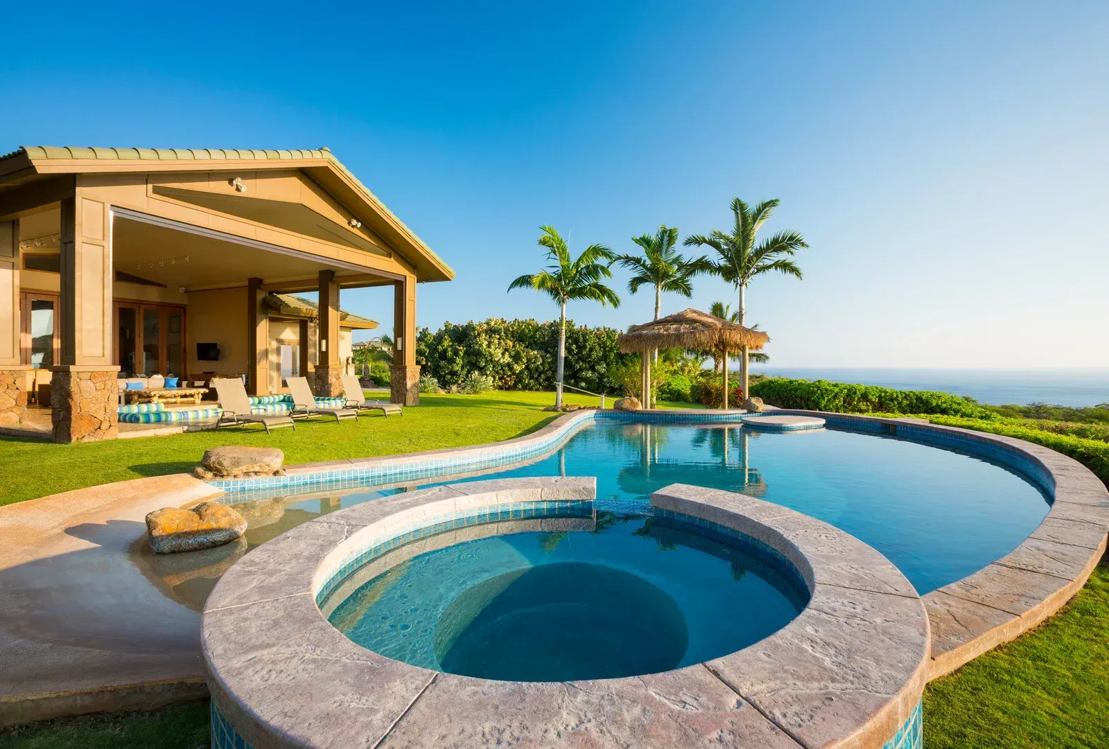 A large swimming pool with a hot tub in front of a house.