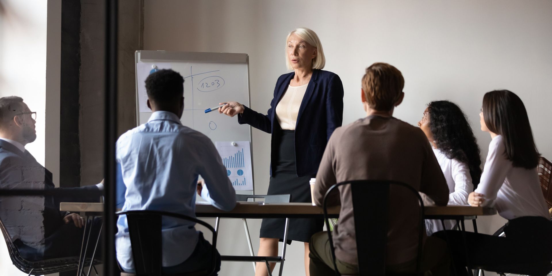 A woman leading a presentation to a group of people in a meeting room.