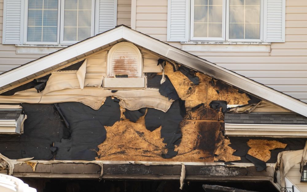 Severely fire-damaged house exterior with burned siding and exposed insulation under the roof