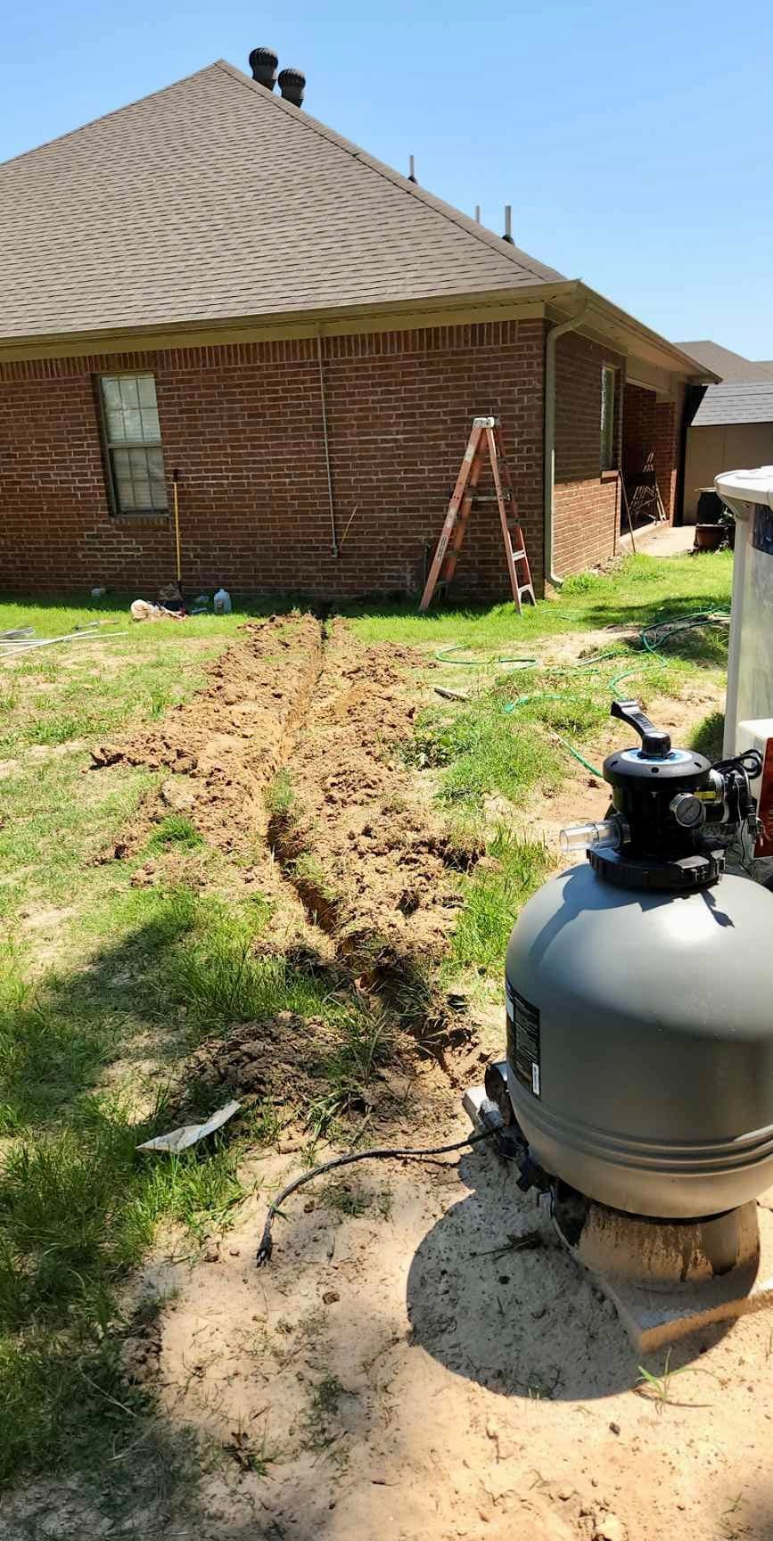 A swimming pool filter is sitting in the dirt in front of a house.