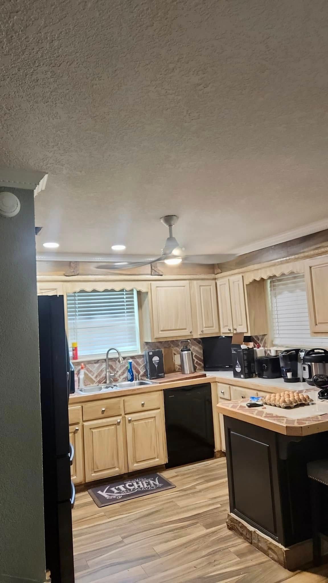 A kitchen with wooden cabinets and black appliances and a ceiling fan.