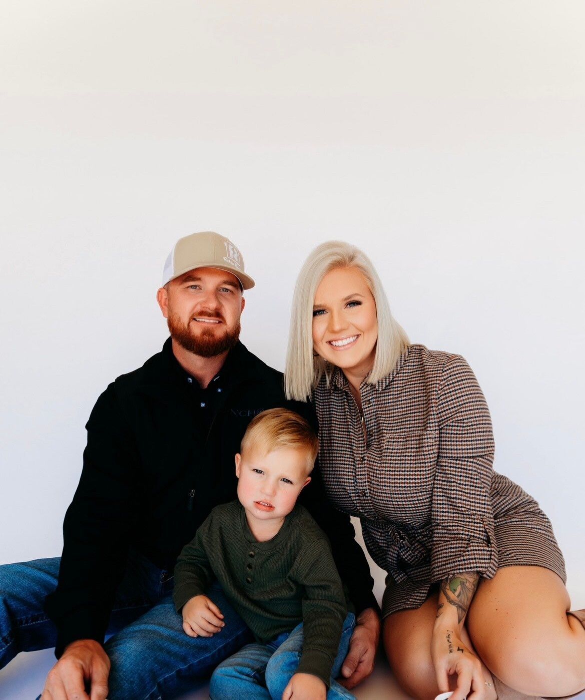 A man , woman and child are posing for a picture while sitting on the floor.