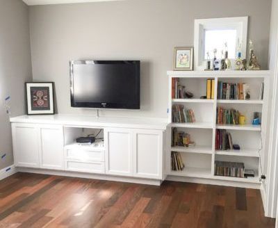 A living room with hardwood floors , white cabinets , a flat screen tv , and a bookshelf.