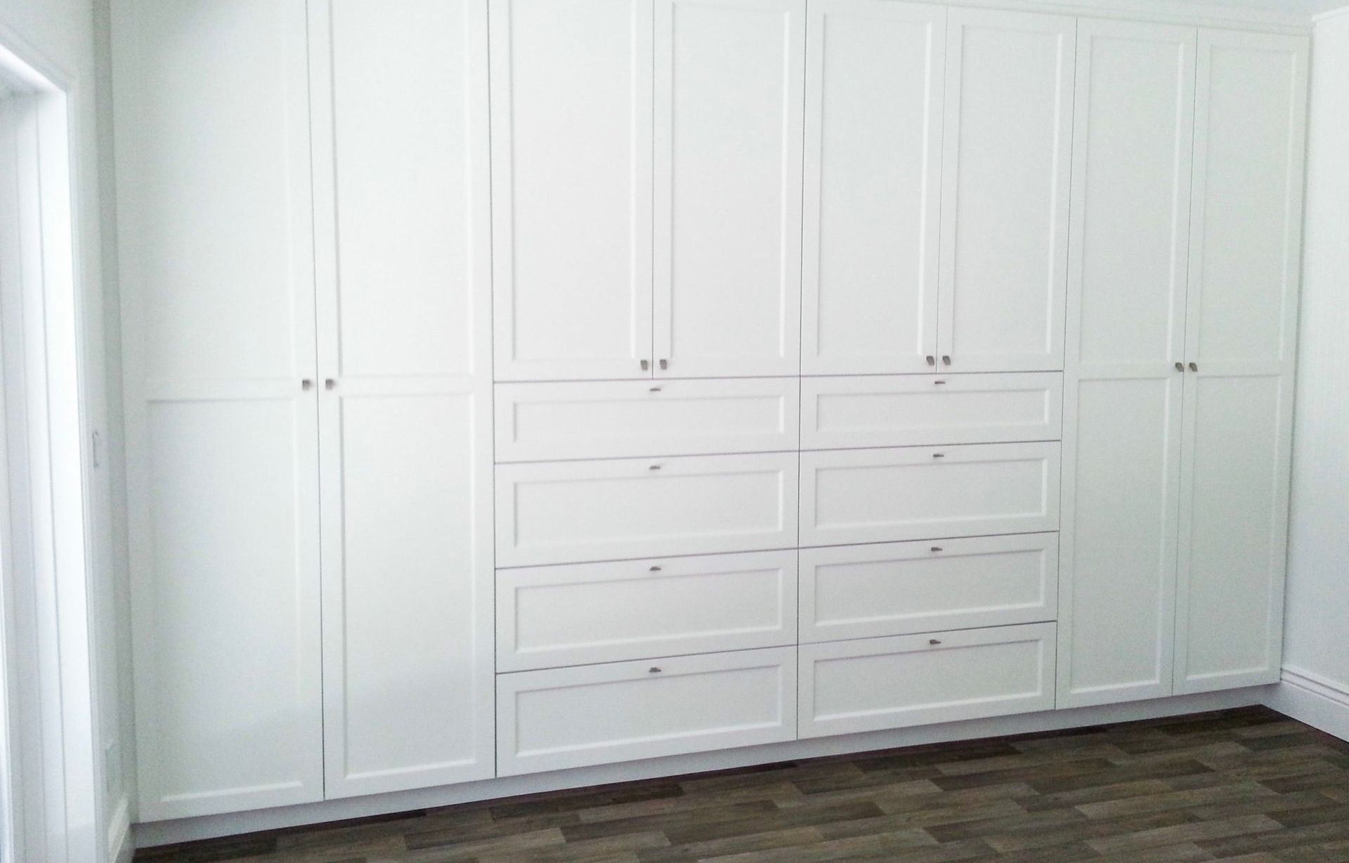 A room with a lot of white cabinets and drawers.