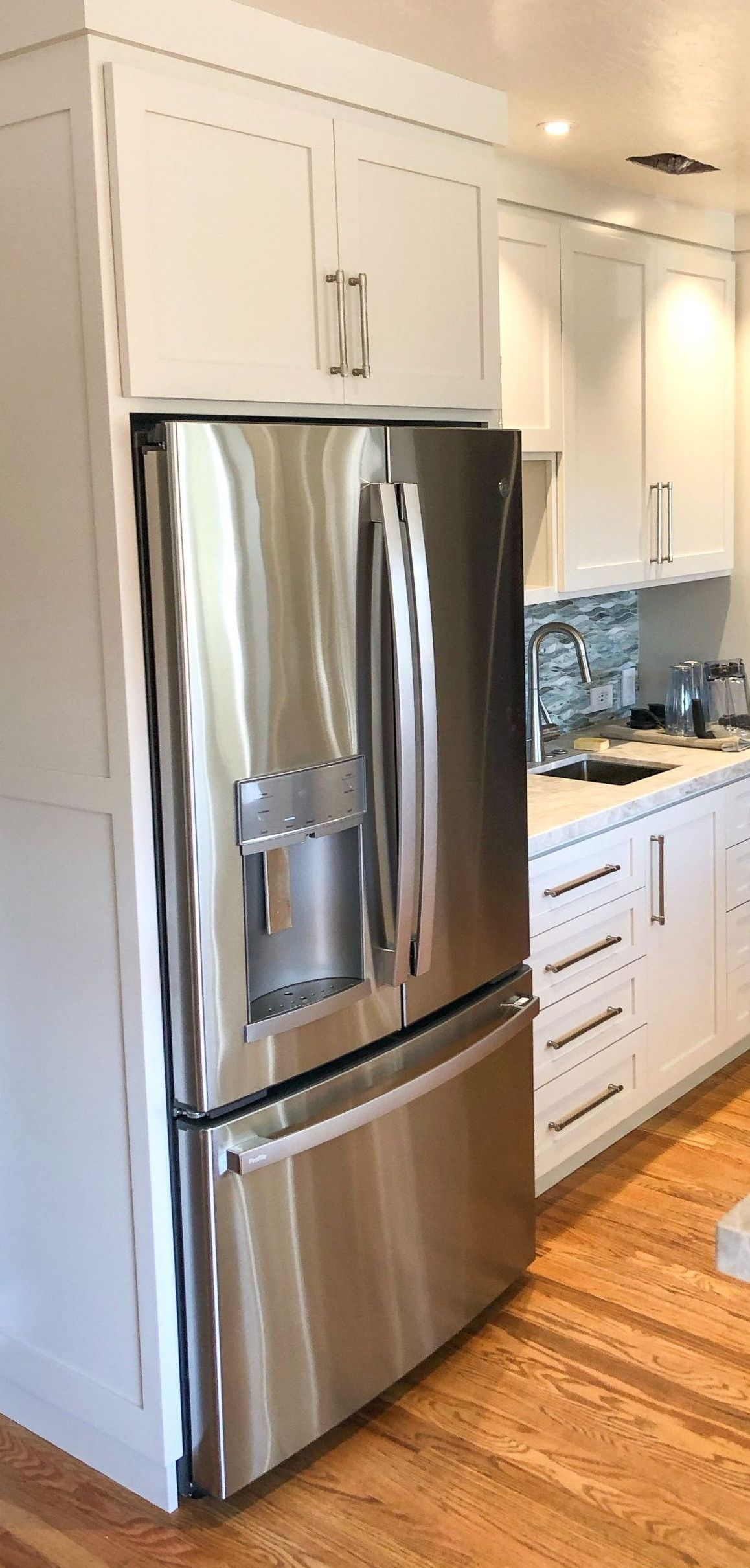 A stainless steel refrigerator in a kitchen with white cabinets and hardwood floors.