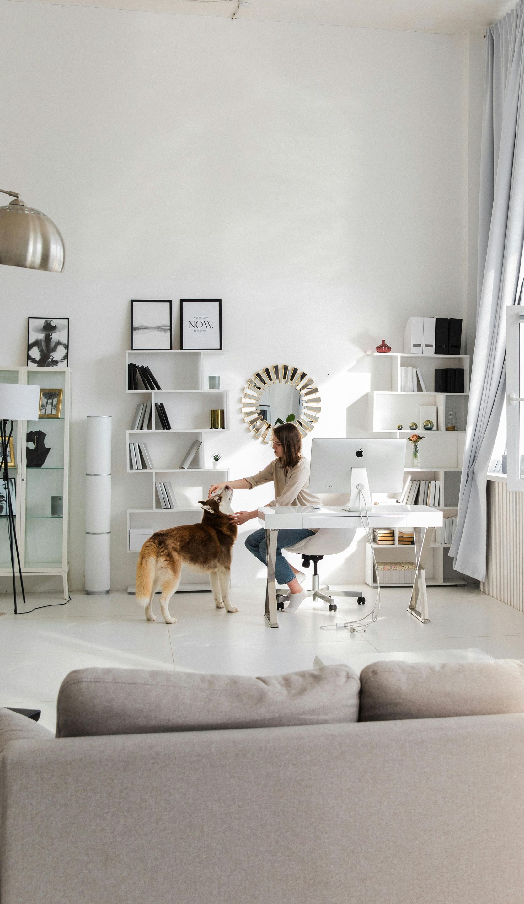 A woman is sitting at a desk with a dog standing next to her.