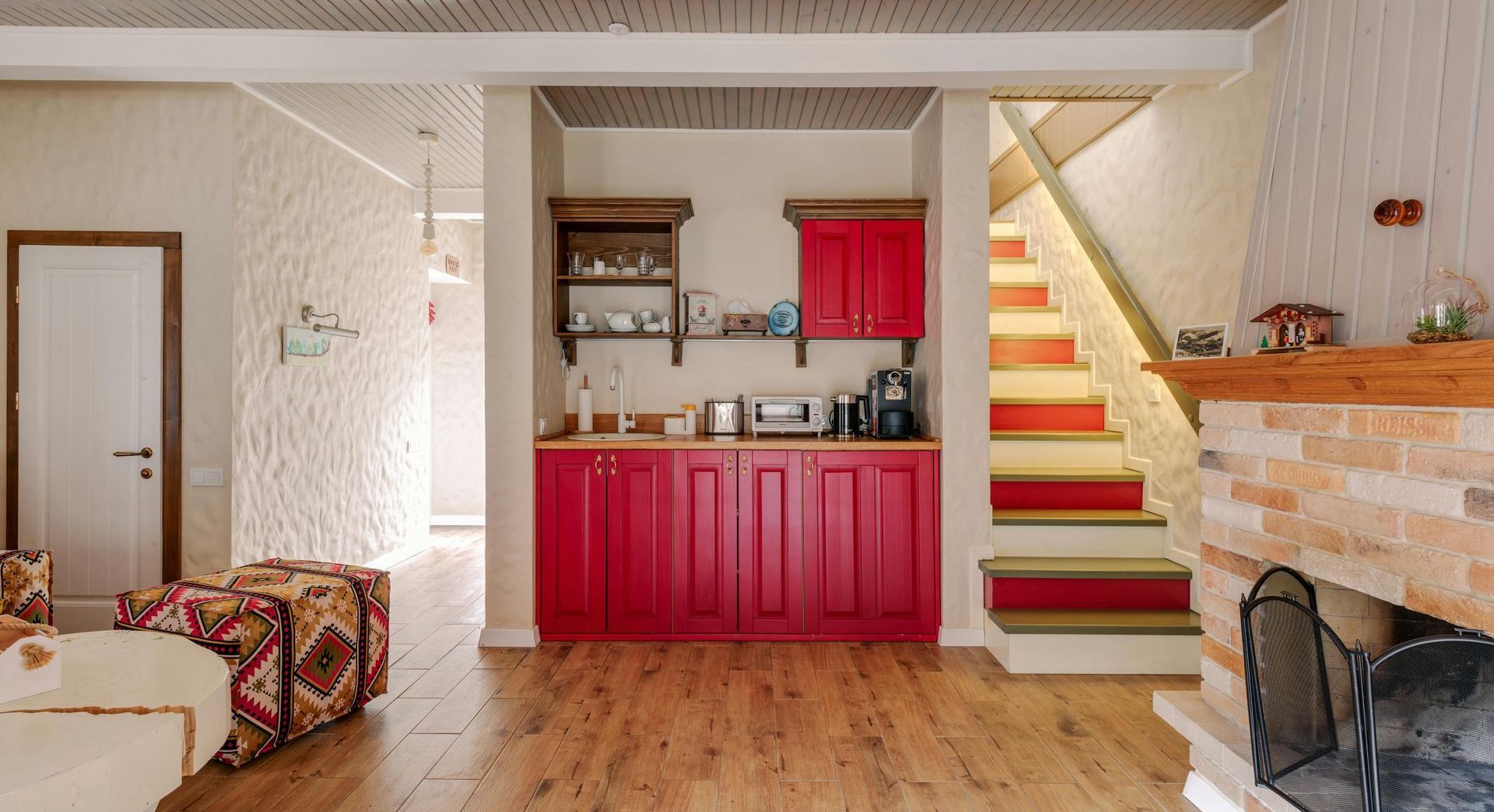 A living room with red cabinets, stairs and a fireplace.