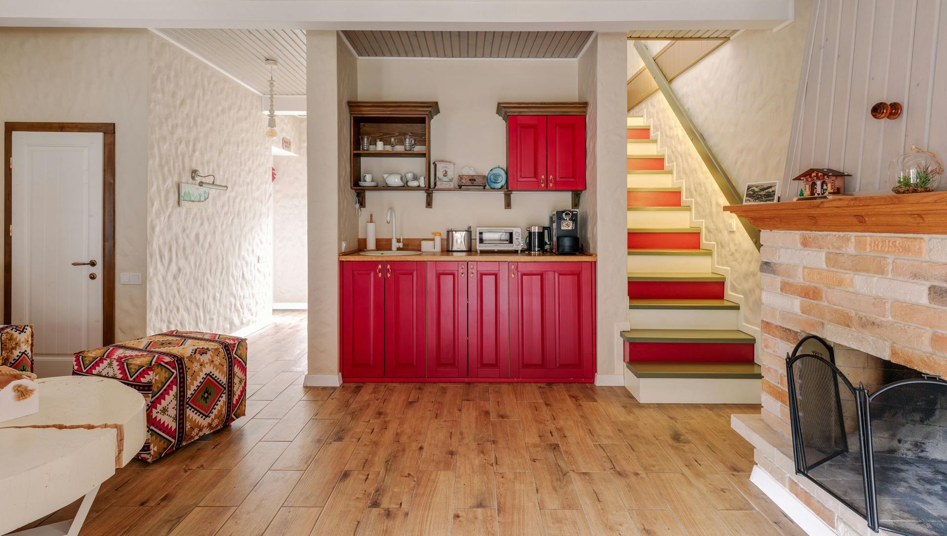 A living room with hardwood floors , red cabinets , stairs and a fireplace.