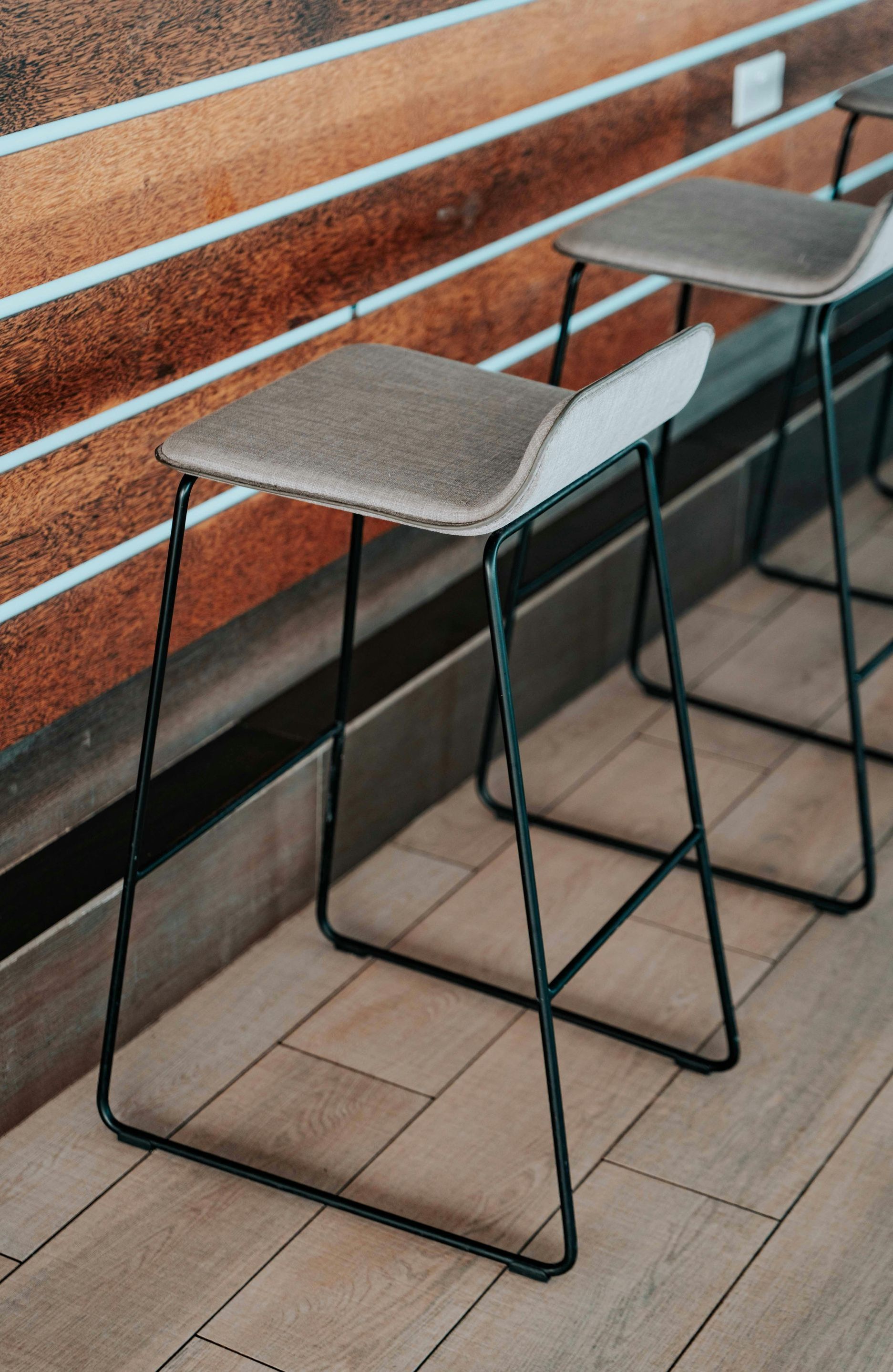 Three bar stools are sitting on a wooden floor in front of a wooden wall.