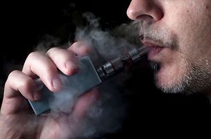 Une personne inhalant à partir d'un stylo vape argenté, expirant une vapeur blanche sur un fond sombre.