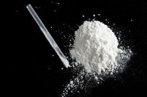 Tas de poudre blanche avec une paille enroulée sur une surface noire.