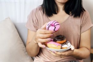 Femme tenant une assiette de beignets colorés, avec un beignet glacé rose dans sa main.